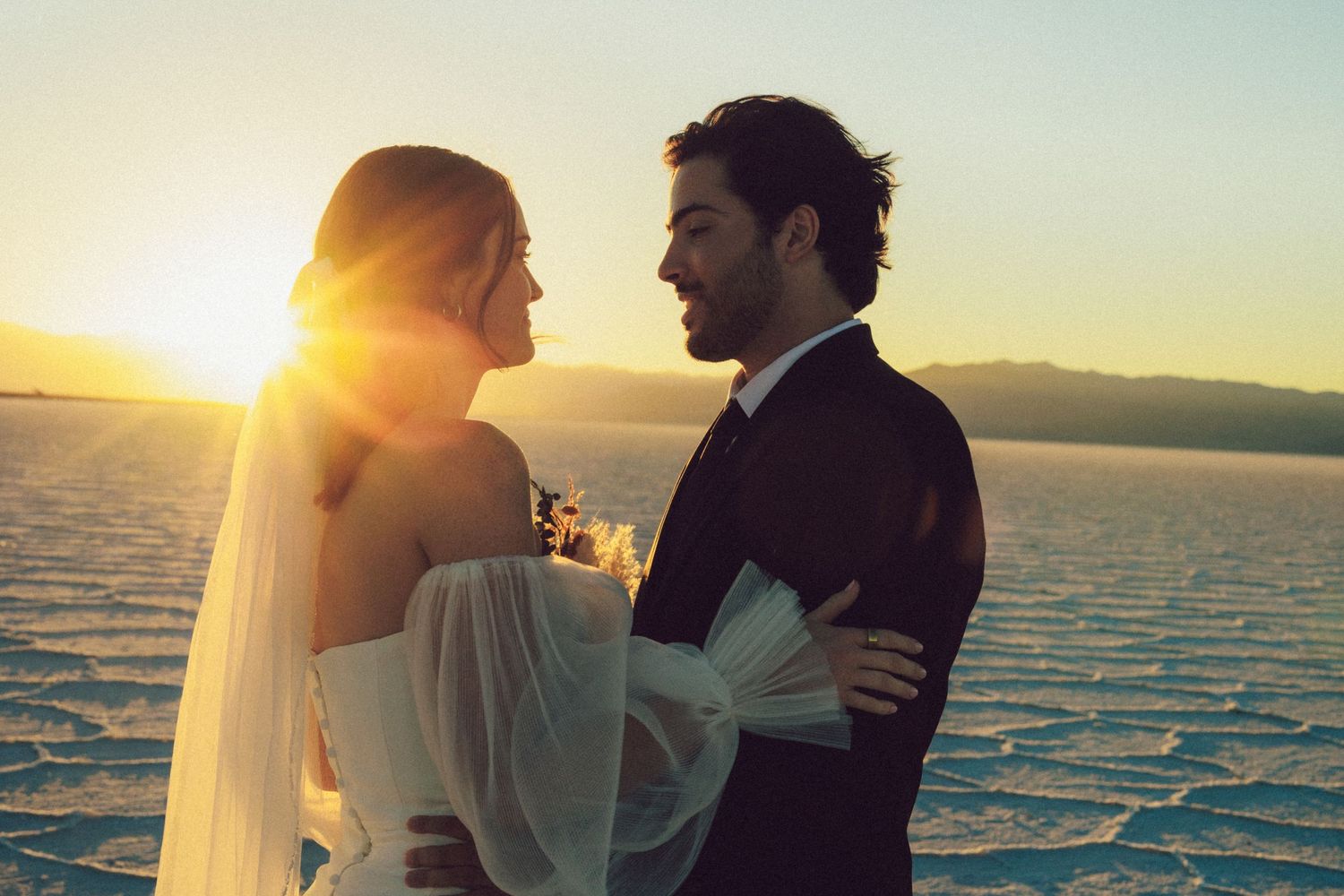 Couple embracing on beach at sunset with golden light streaming through.