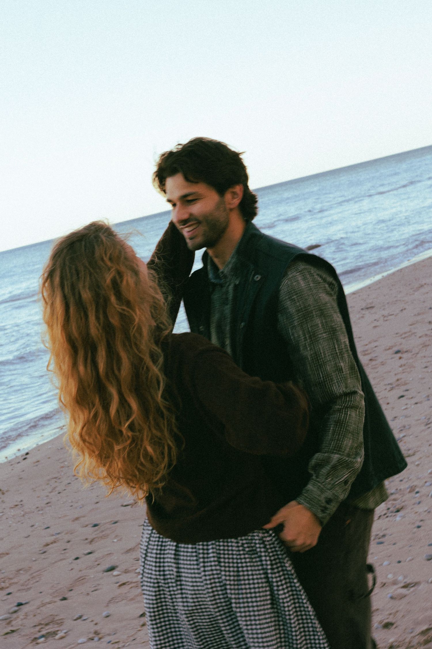 Romantic couple embracing on sandy beach with ocean waves in background.