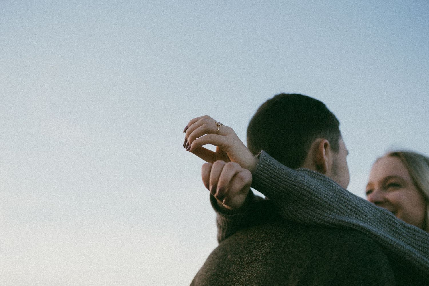 Close-up view of two people embracing against a light blue sky background.