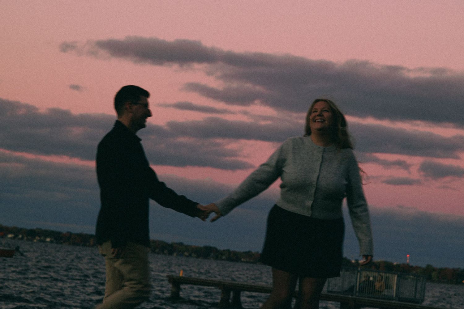 Silhouettes against a pink sunset sky over water.