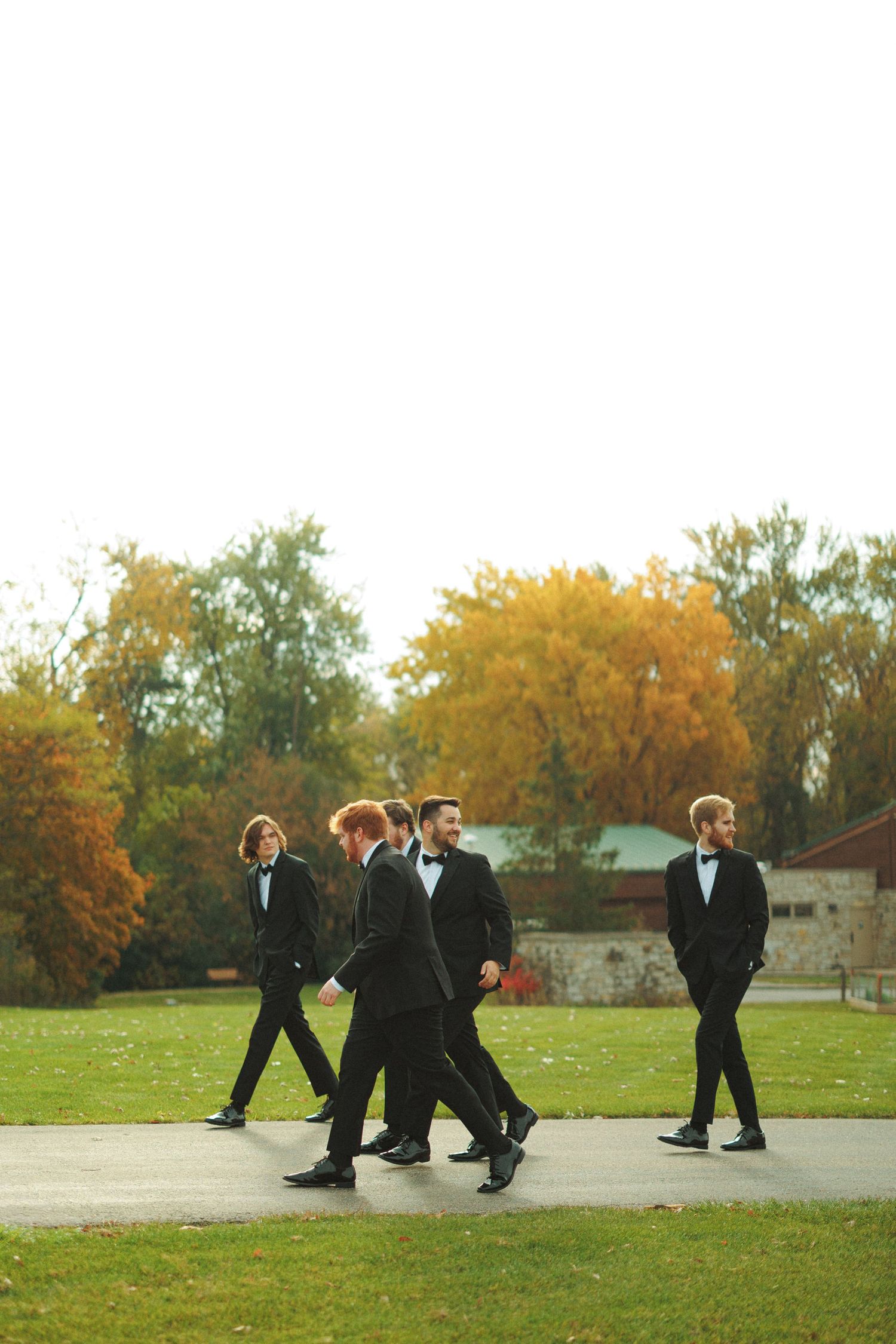 Groomsmen walking in formation across an autumn field wearing black tuxedos.