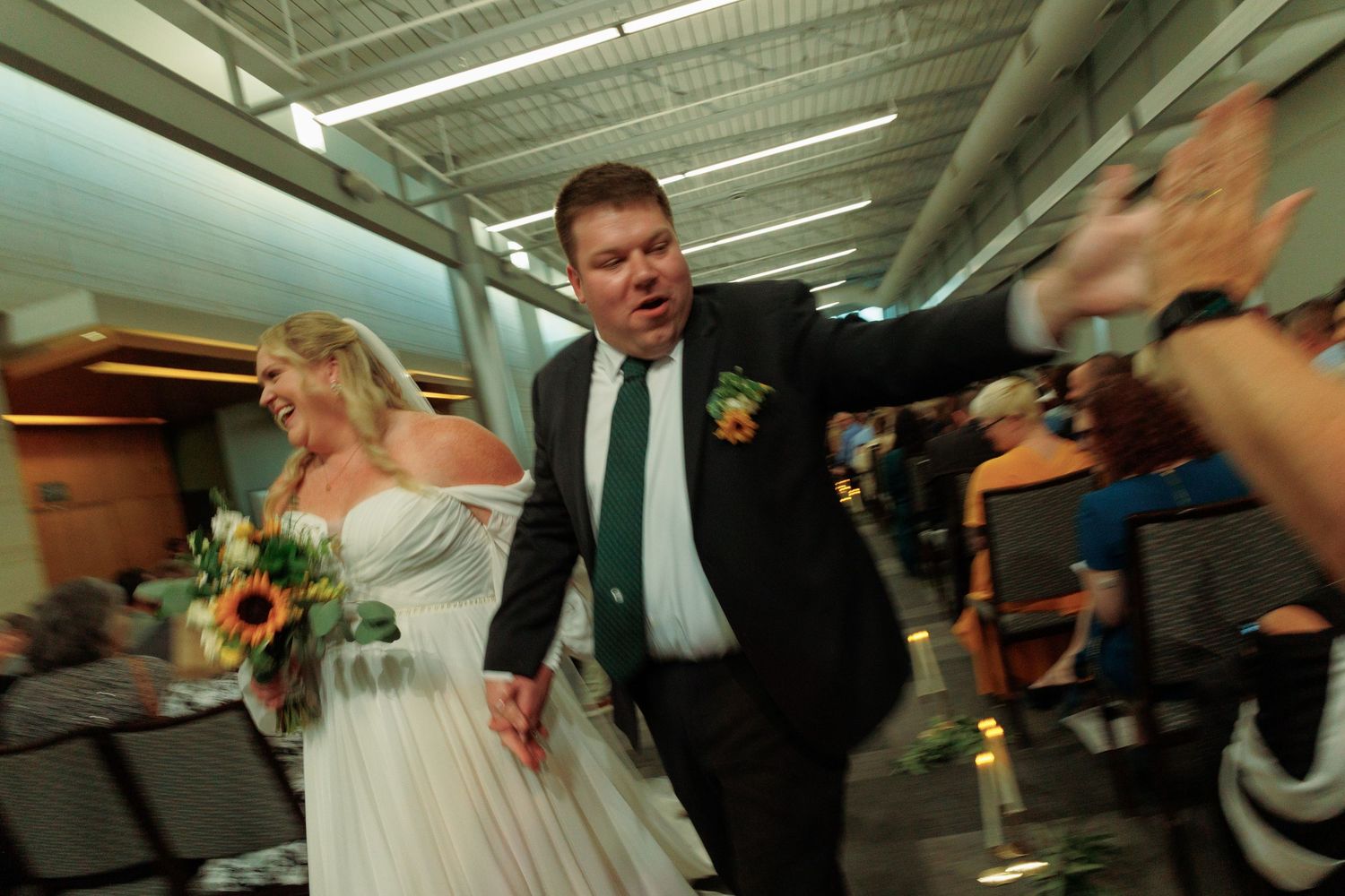 Wedding guests celebrate and dance in a brightly lit indoor venue.
