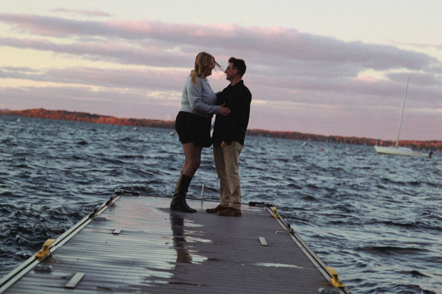 A couple shares a romantic moment while standing on a dock at sunset over a lake.