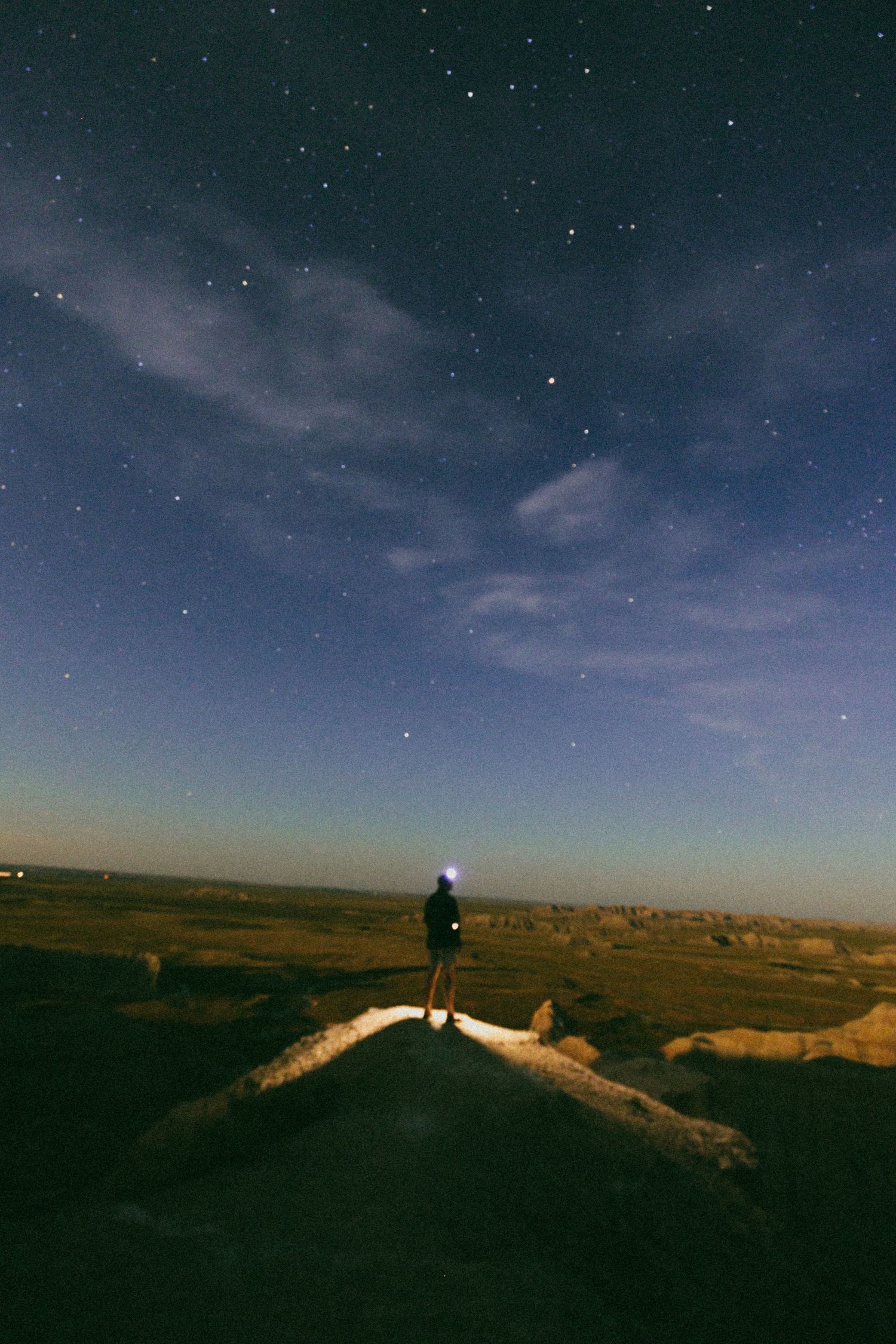 Starlit night sky over a desert landscape with distant lights creating a serene atmosphere.