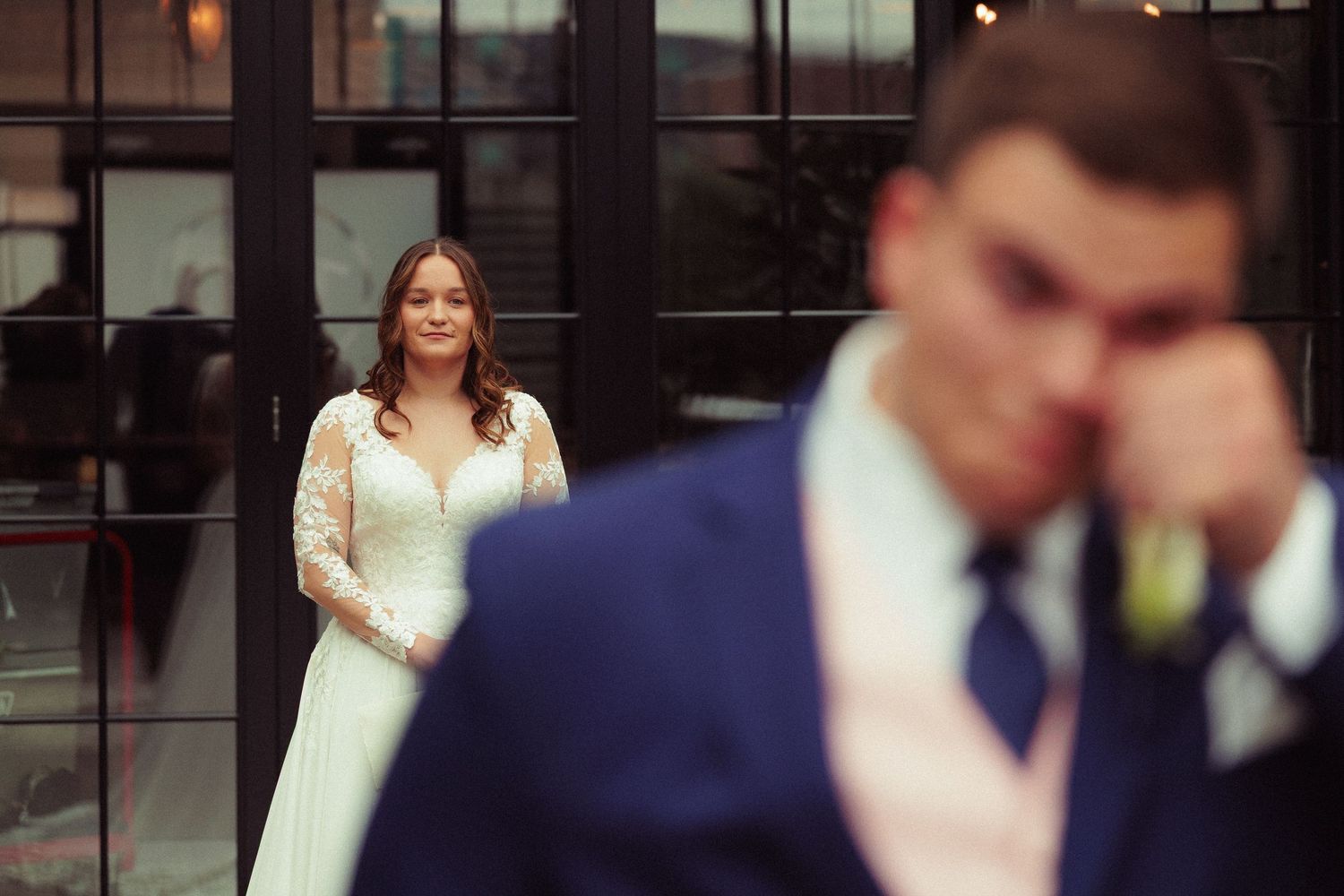 Wedding party members in formal attire gather indoors near large windows.