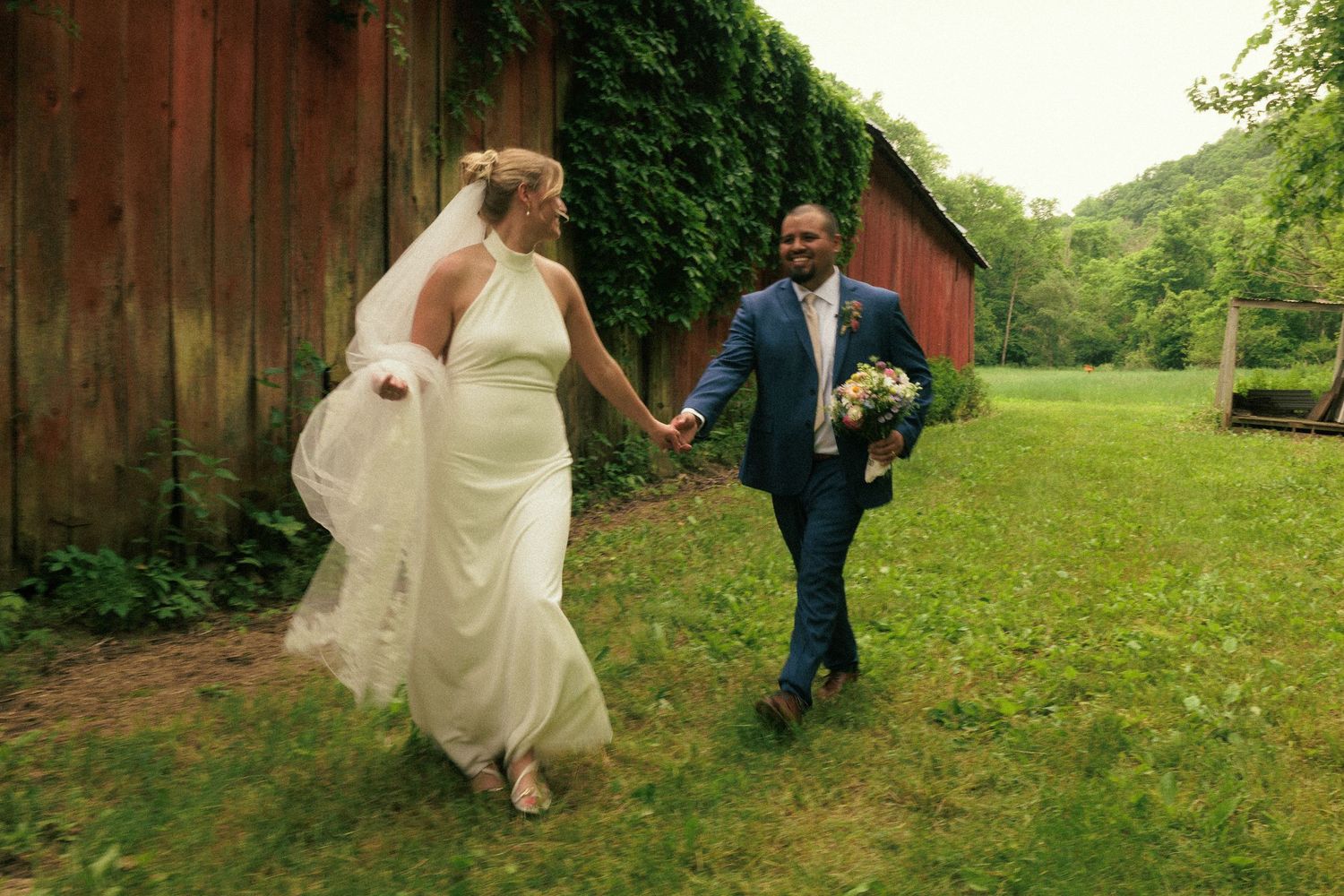 A rustic barn wedding celebration with guests mingling outside on grass.
