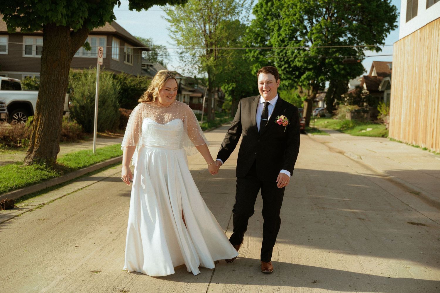 Wedding couple walking together on sidewalk outside brick building.