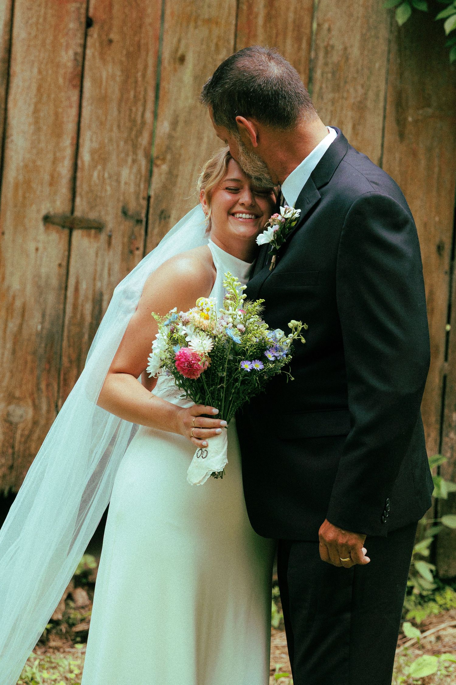 Romantic wedding couple sharing tender moments against a rustic wooden fence backdrop.
