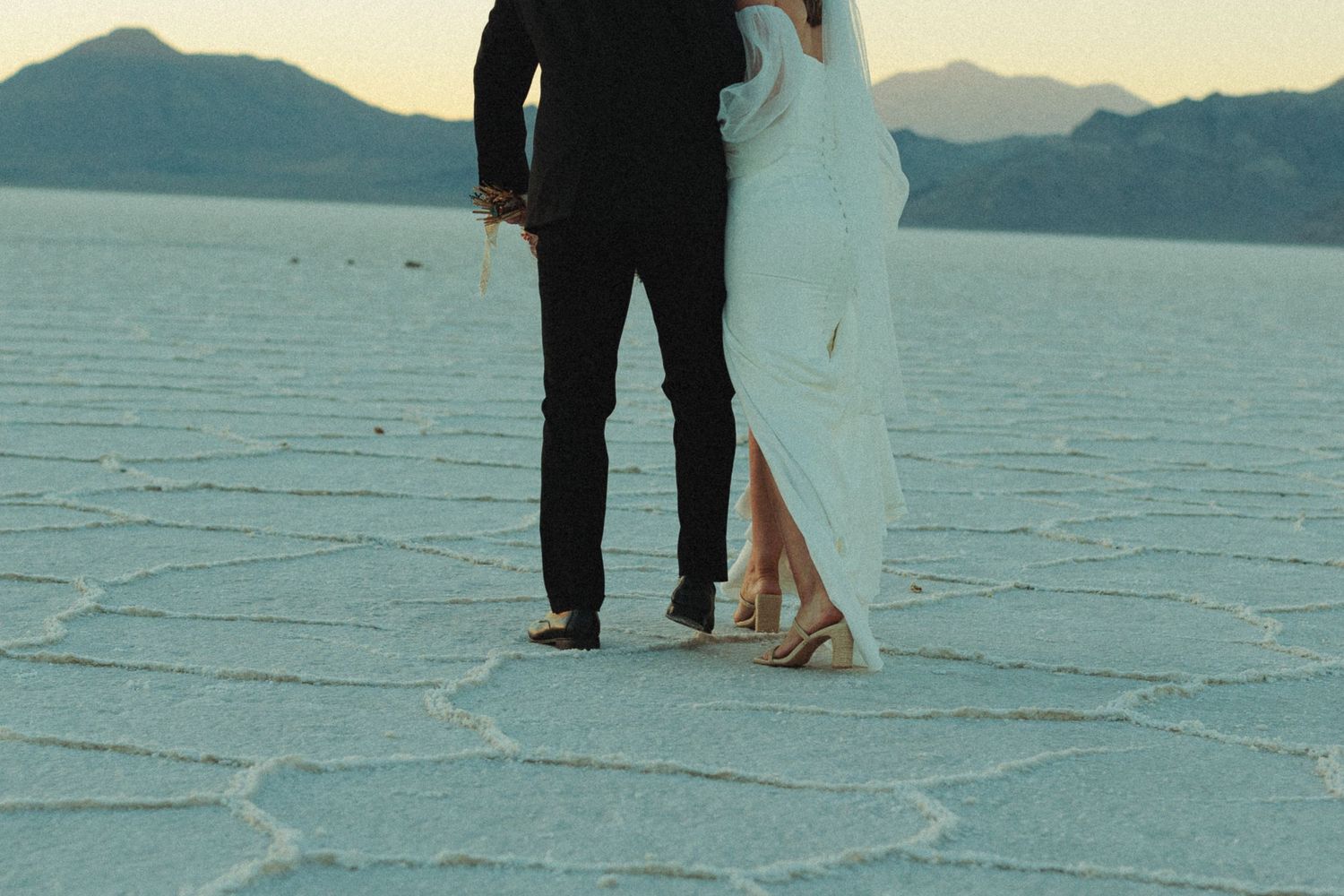Silhouettes of newlyweds standing on vast utah salt flats with mountains in background.