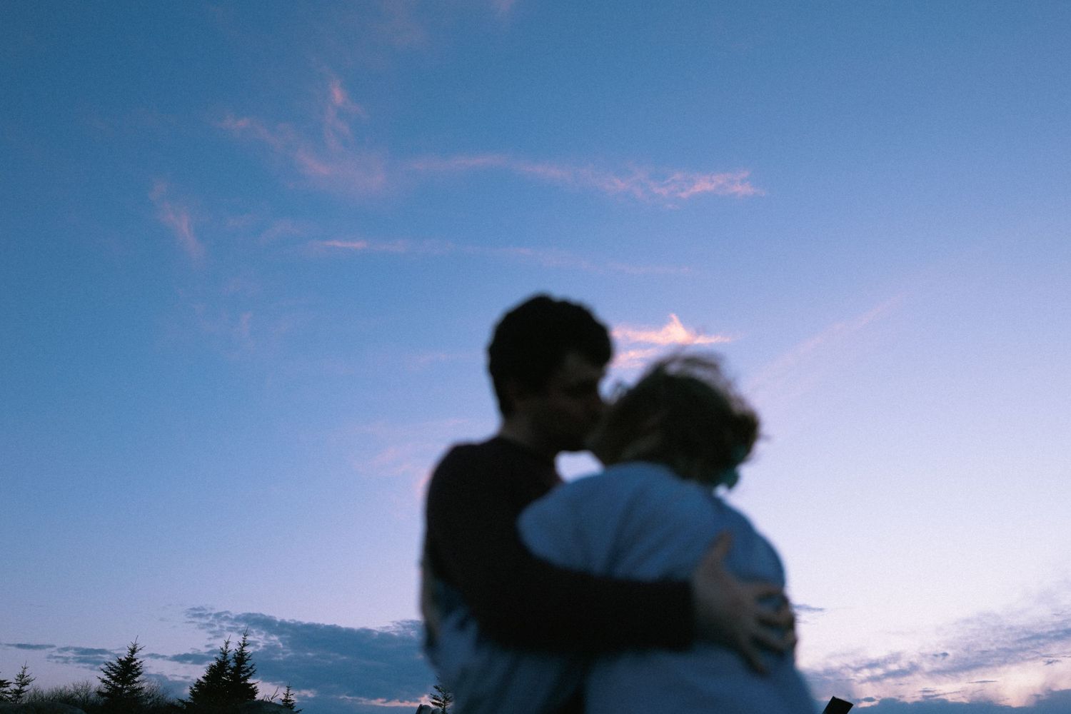 Romantic couple sharing a kiss silhouetted against a vibrant blue twilight sky at dusk.