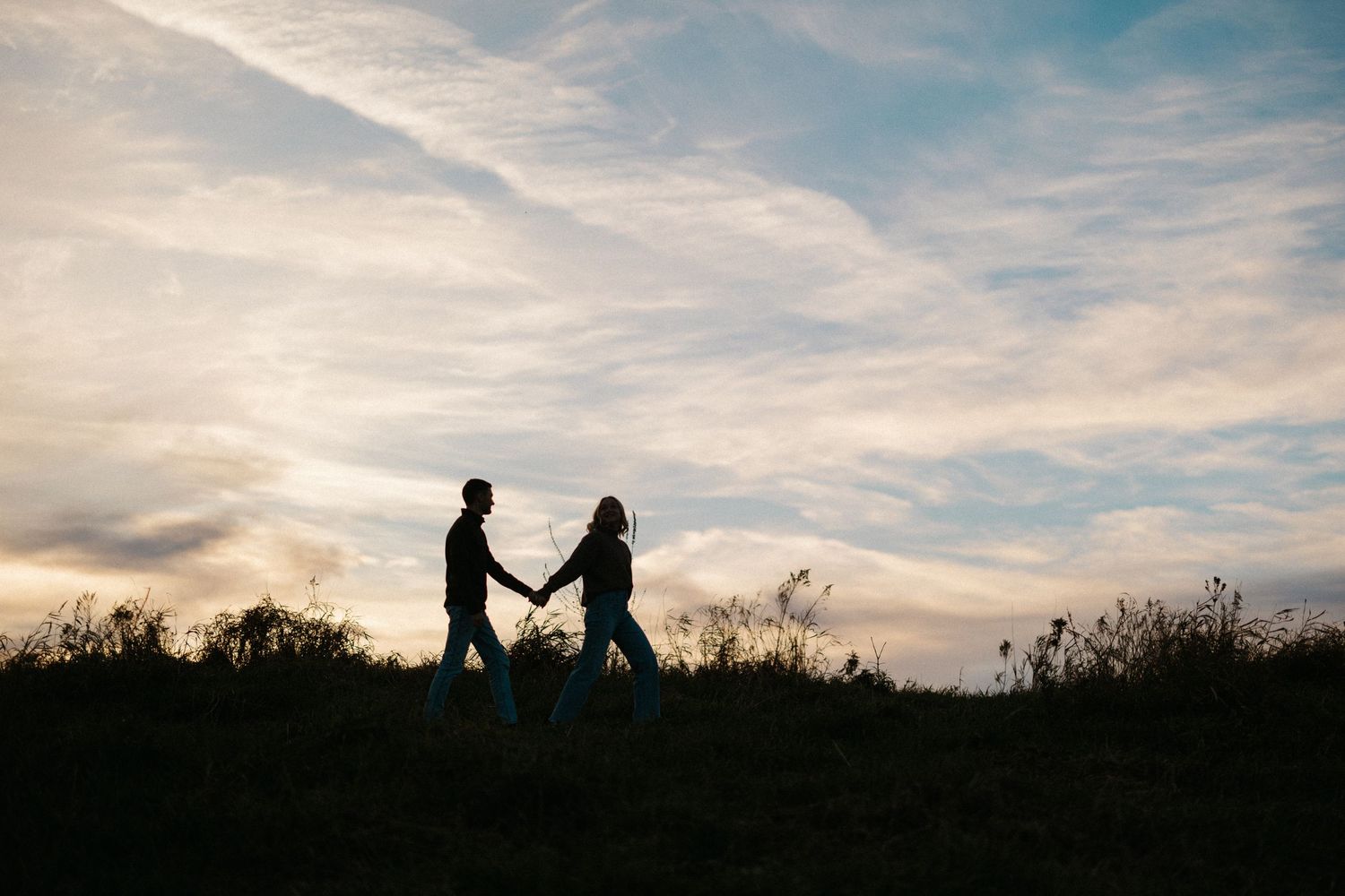 Silhouettes of a couple against a dramatic sunset sky with wispy clouds.