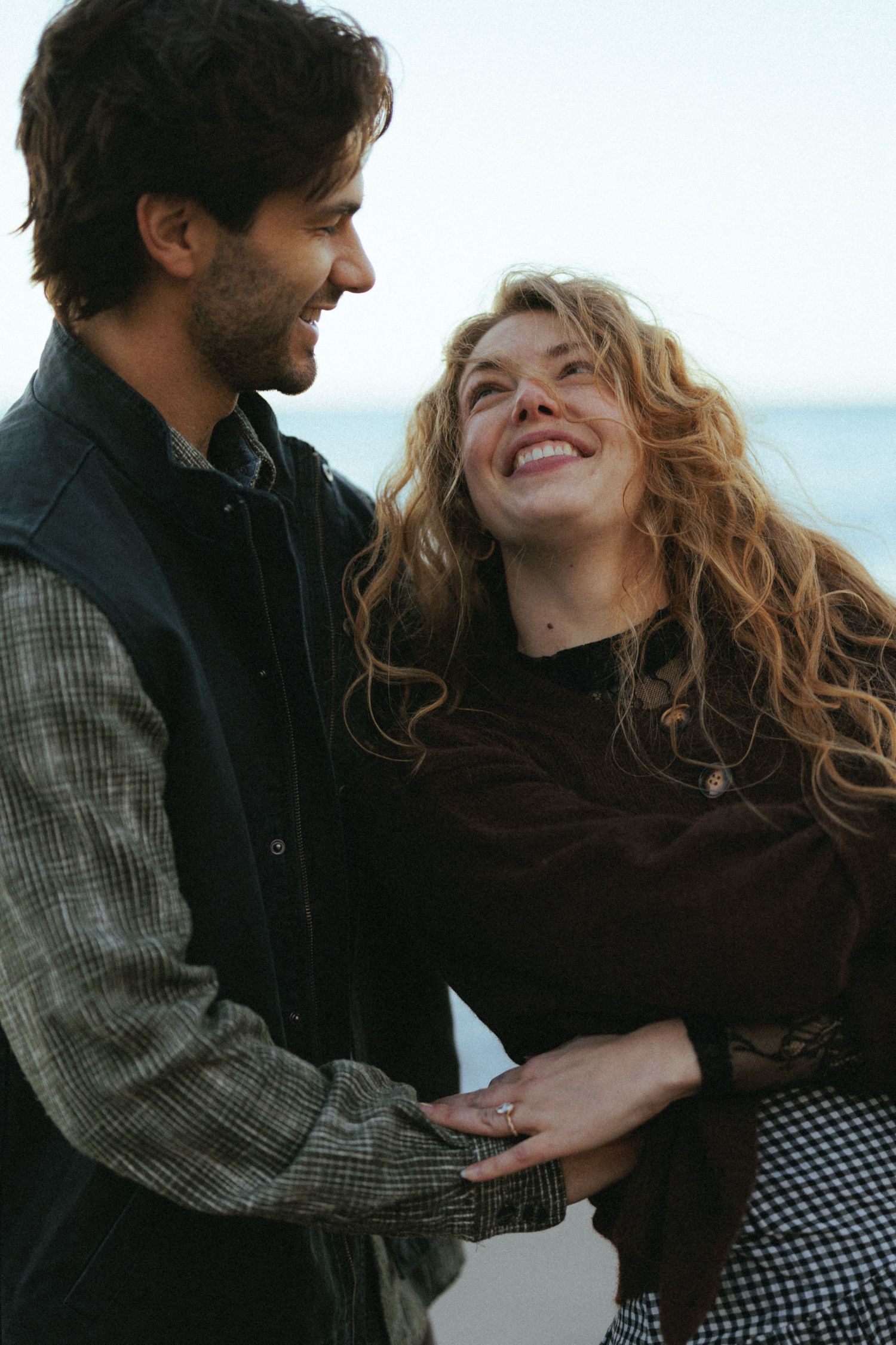 Joyful couple sharing a laugh together on a beach with ocean in background.
