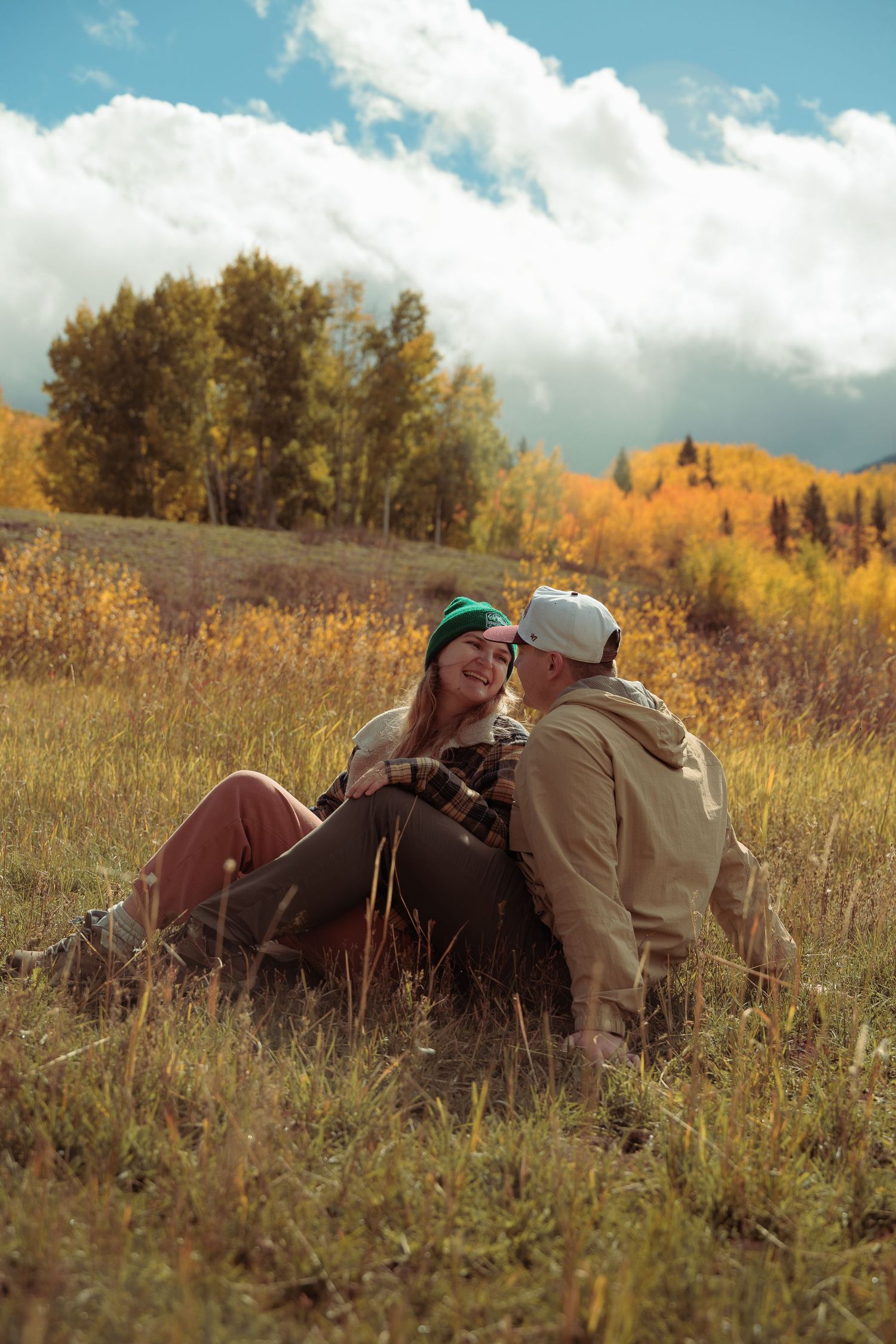 Couple lying in golden grass field with mountains in background.