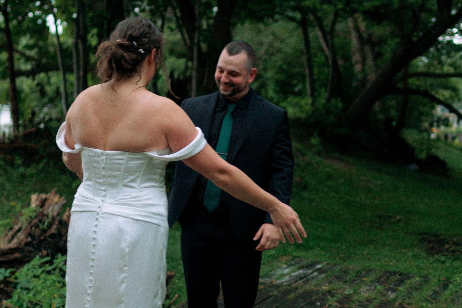 A couple in wedding attire share a playful moment outdoors in a lush green garden setting.