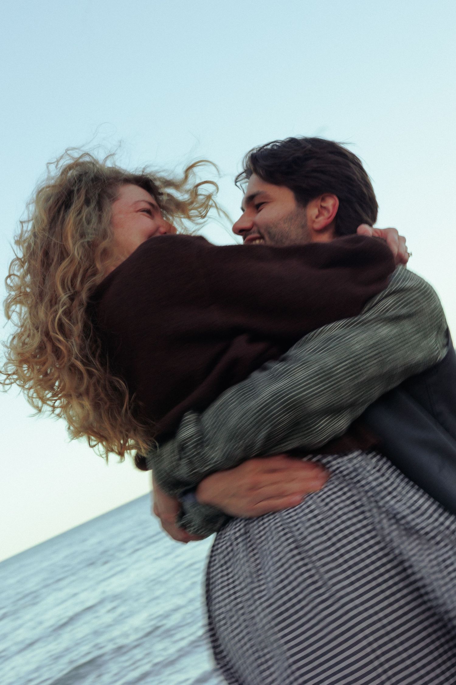 A joyful embrace captured against an ocean backdrop at sunset.
