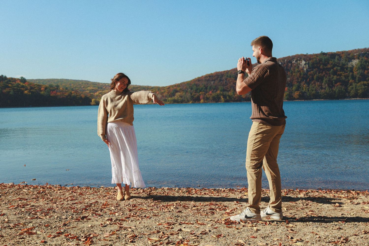 A couple poses for photos near a scenic autumn lake.