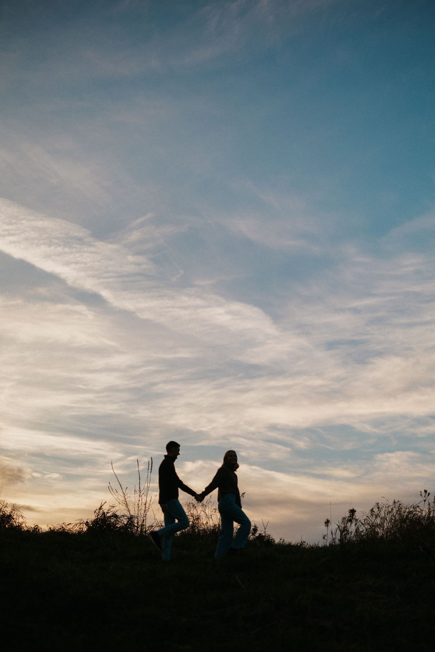 Silhouettes of people against dramatic sunset sky with wispy clouds.