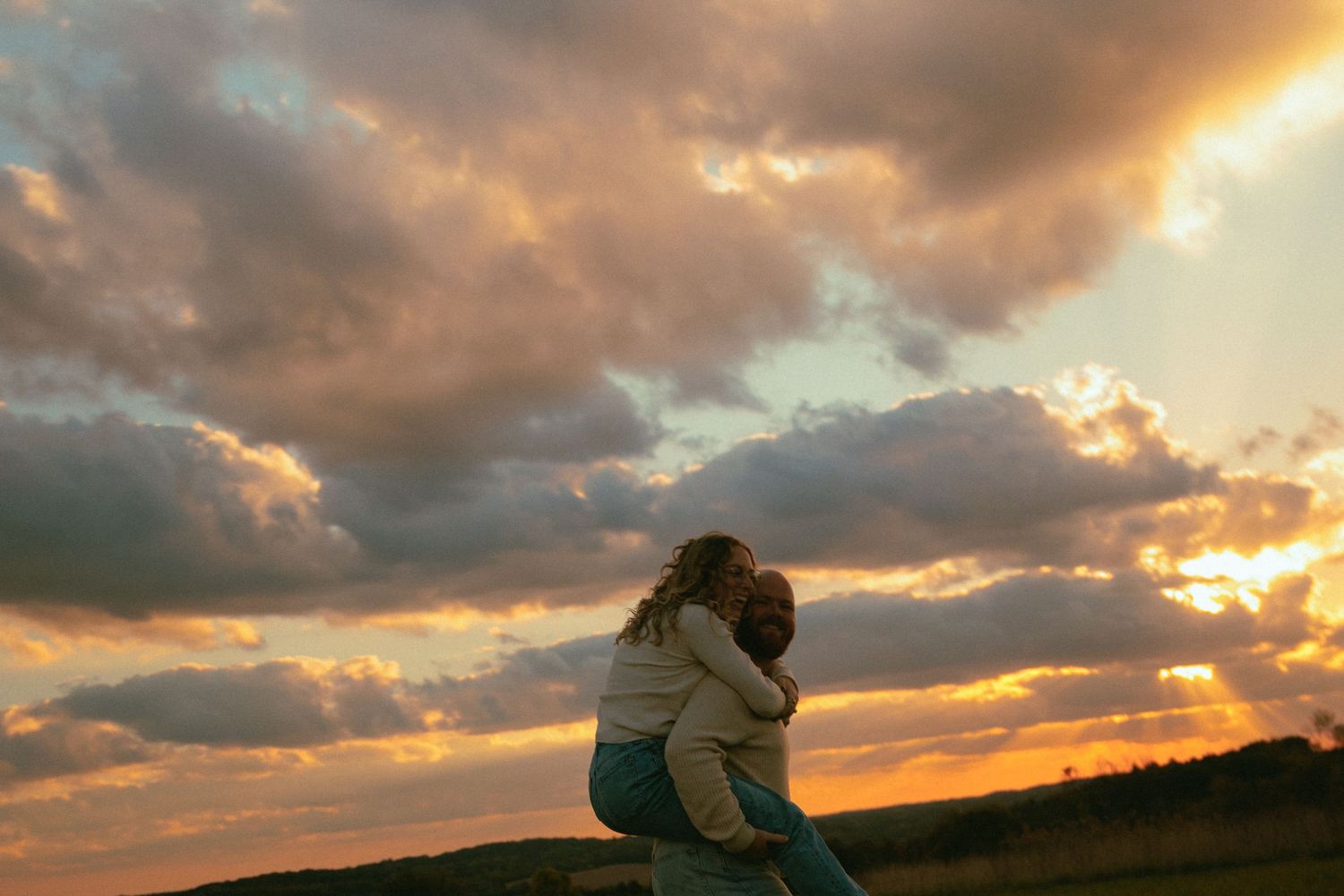 A dramatic sunset illuminates a silhouetted figure sitting on a hillside against an orange and purple cloudy sky.