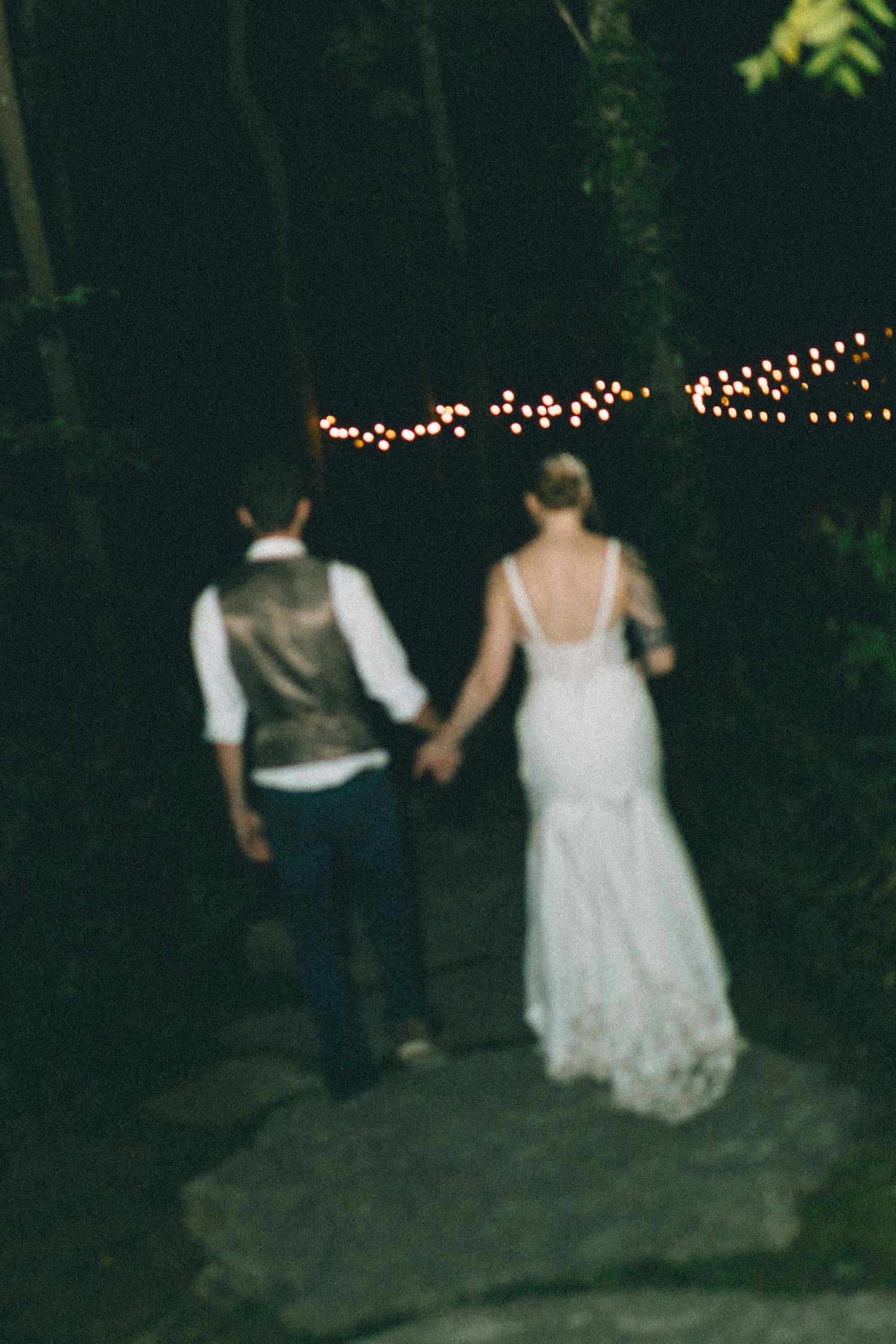 Couple walks along path at night under romantic string lights.