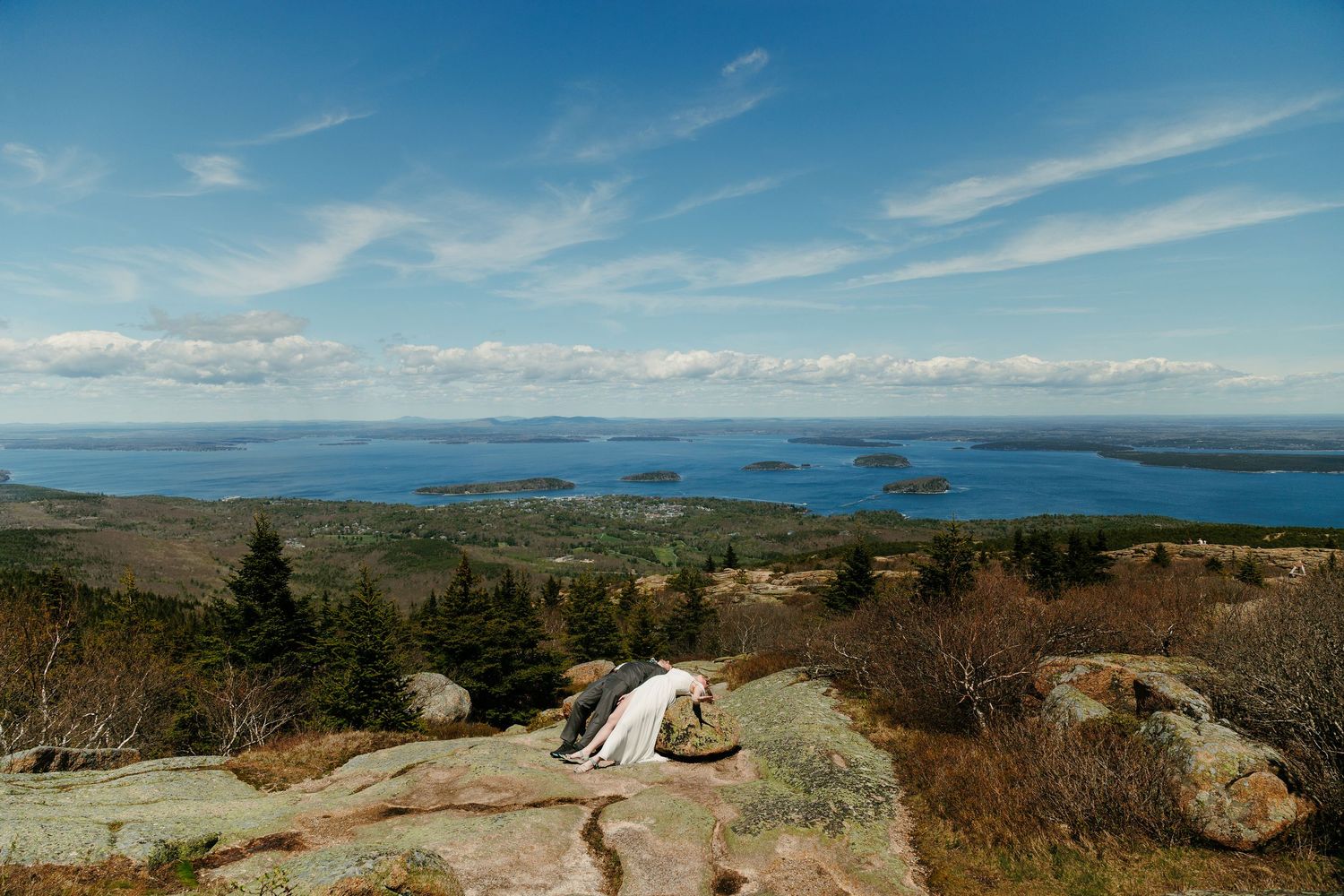 Panoramic view from Cadillac Mountain in Acadia National Park, showing rocky terrain, evergreen trees, and island-dotted blue waters.