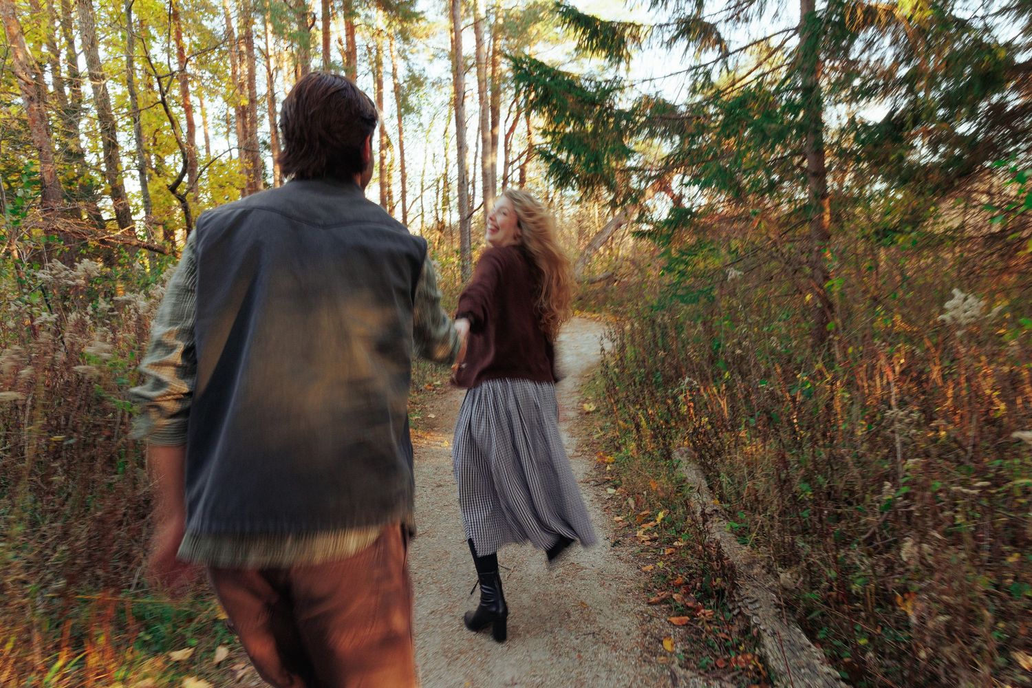 Couple walking together on a forest path surrounded by autumn foliage.