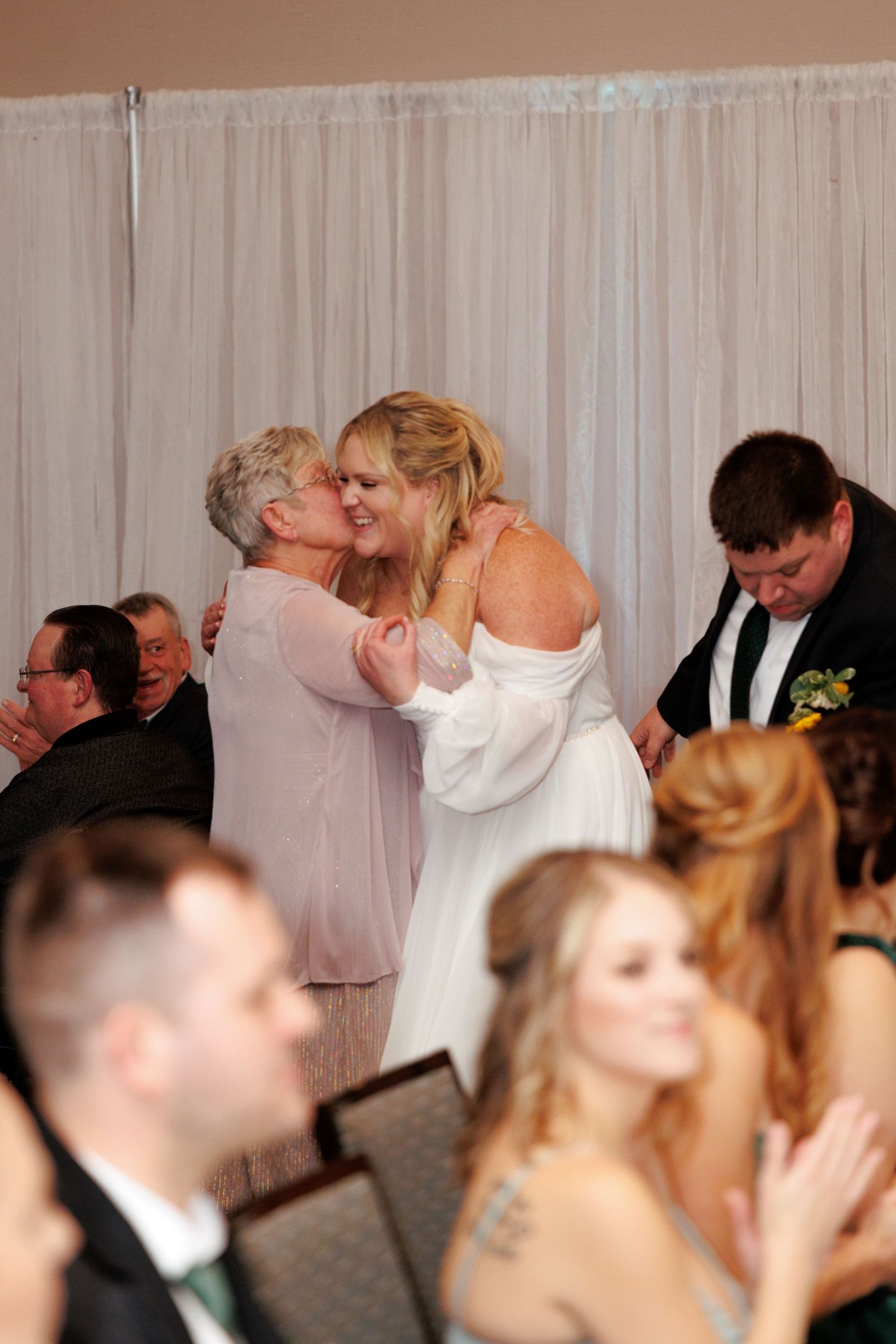 Wedding reception guests dancing and celebrating in a banquet hall with white curtains.