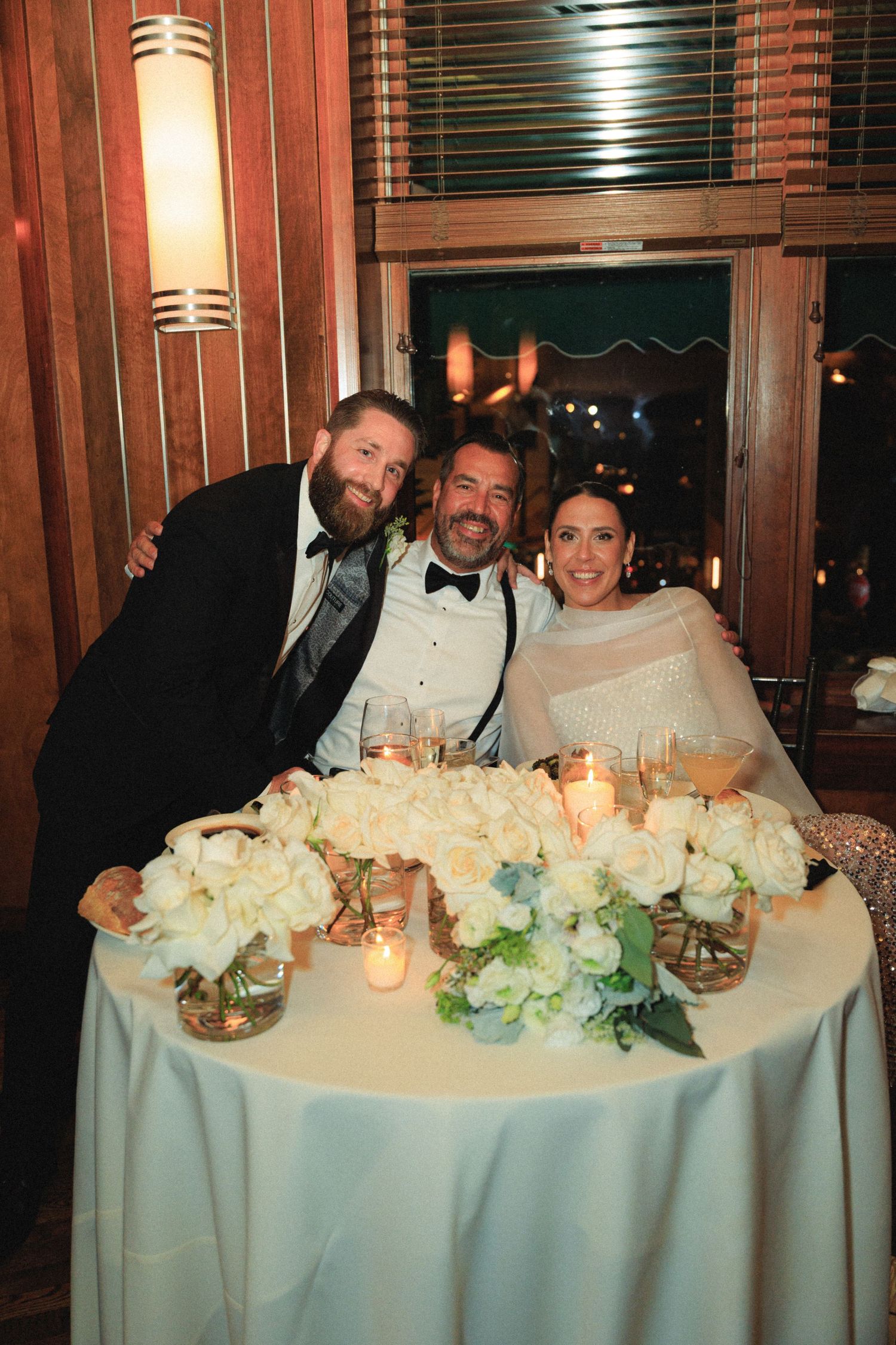Elegant wedding reception table with white floral centerpieces and candlelight.