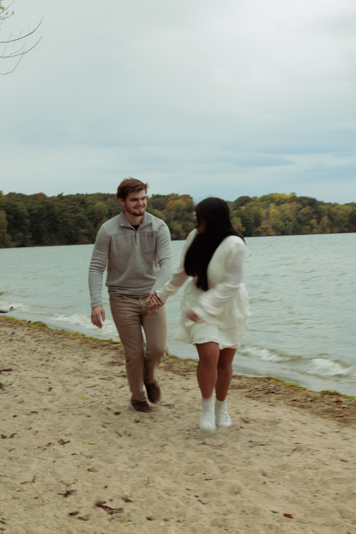 Couple walking and playing together on a beach near the water.
