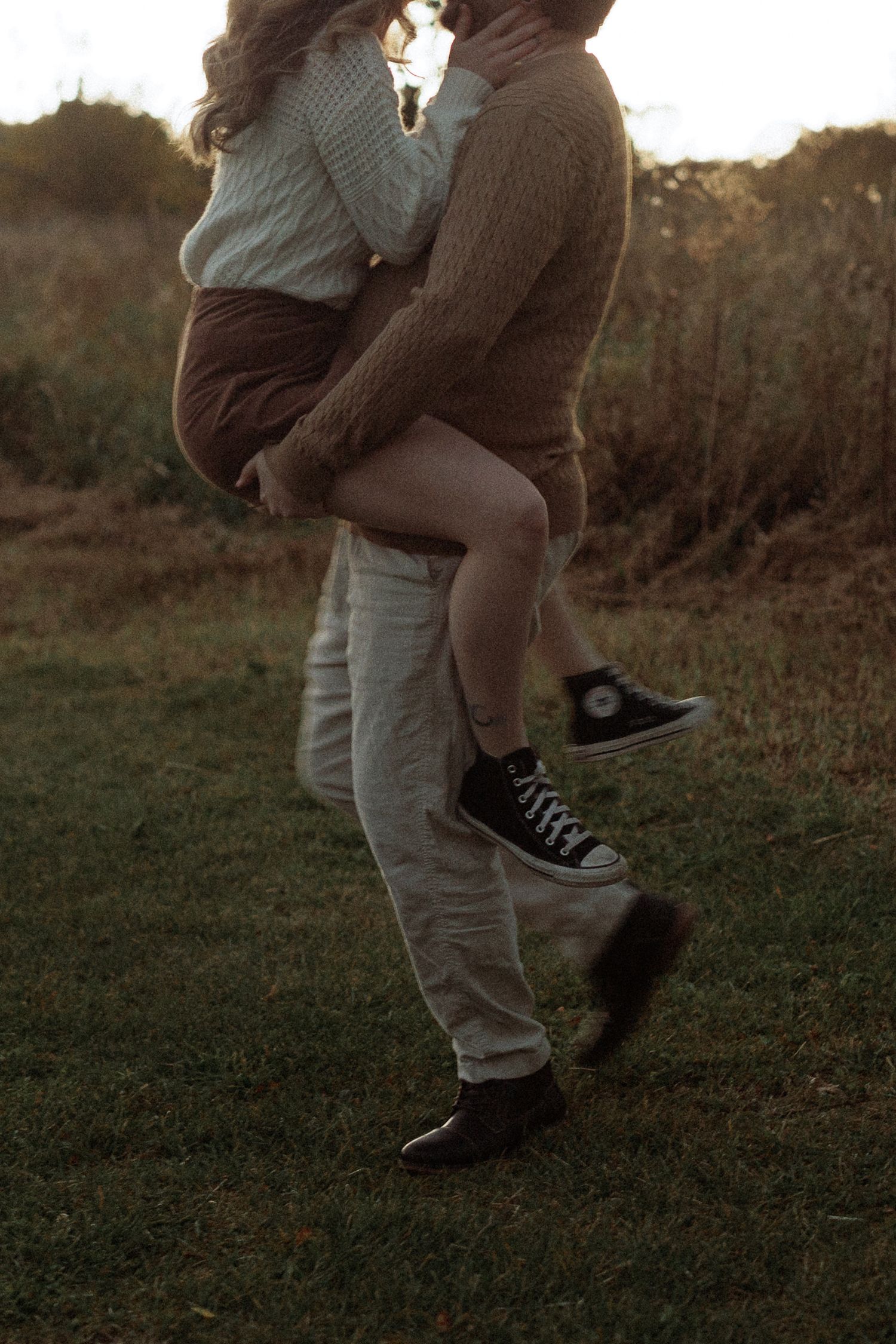 Close-up view of legs and black Converse sneakers during an intimate outdoor photoshoot at golden hour.