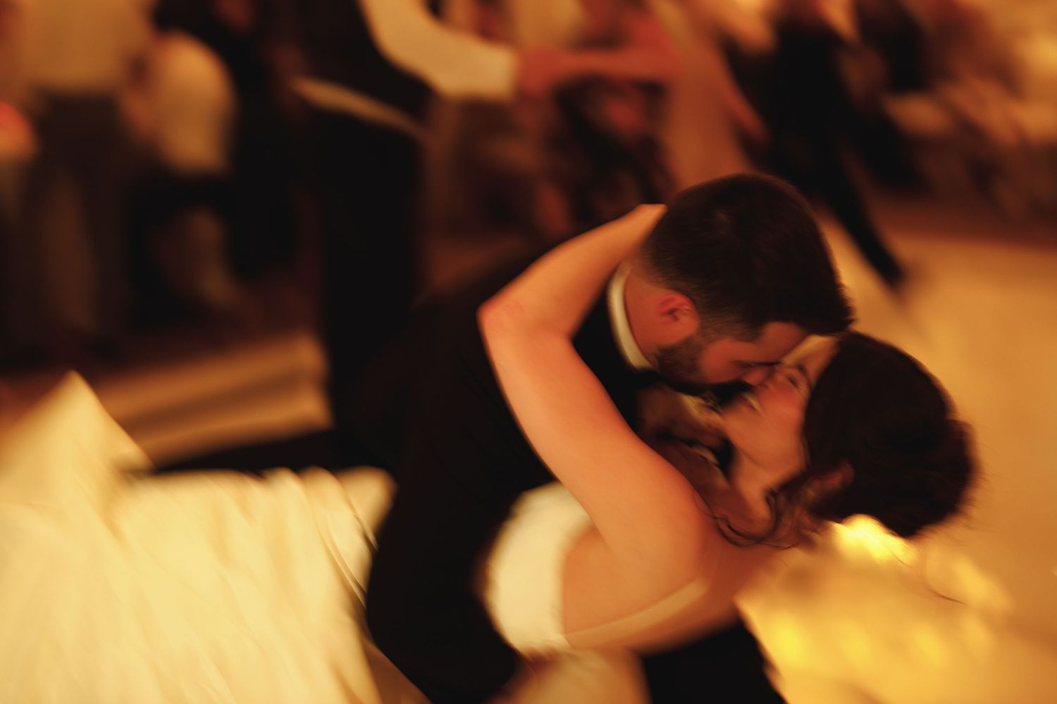 Couples dancing in warm lighting during an indoor wedding reception celebration.