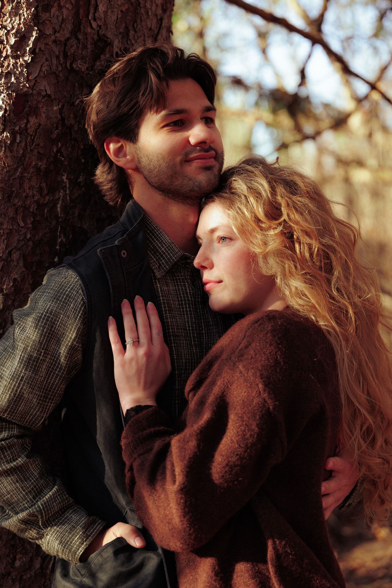 Romantic embrace against a tree trunk in autumn forest setting.