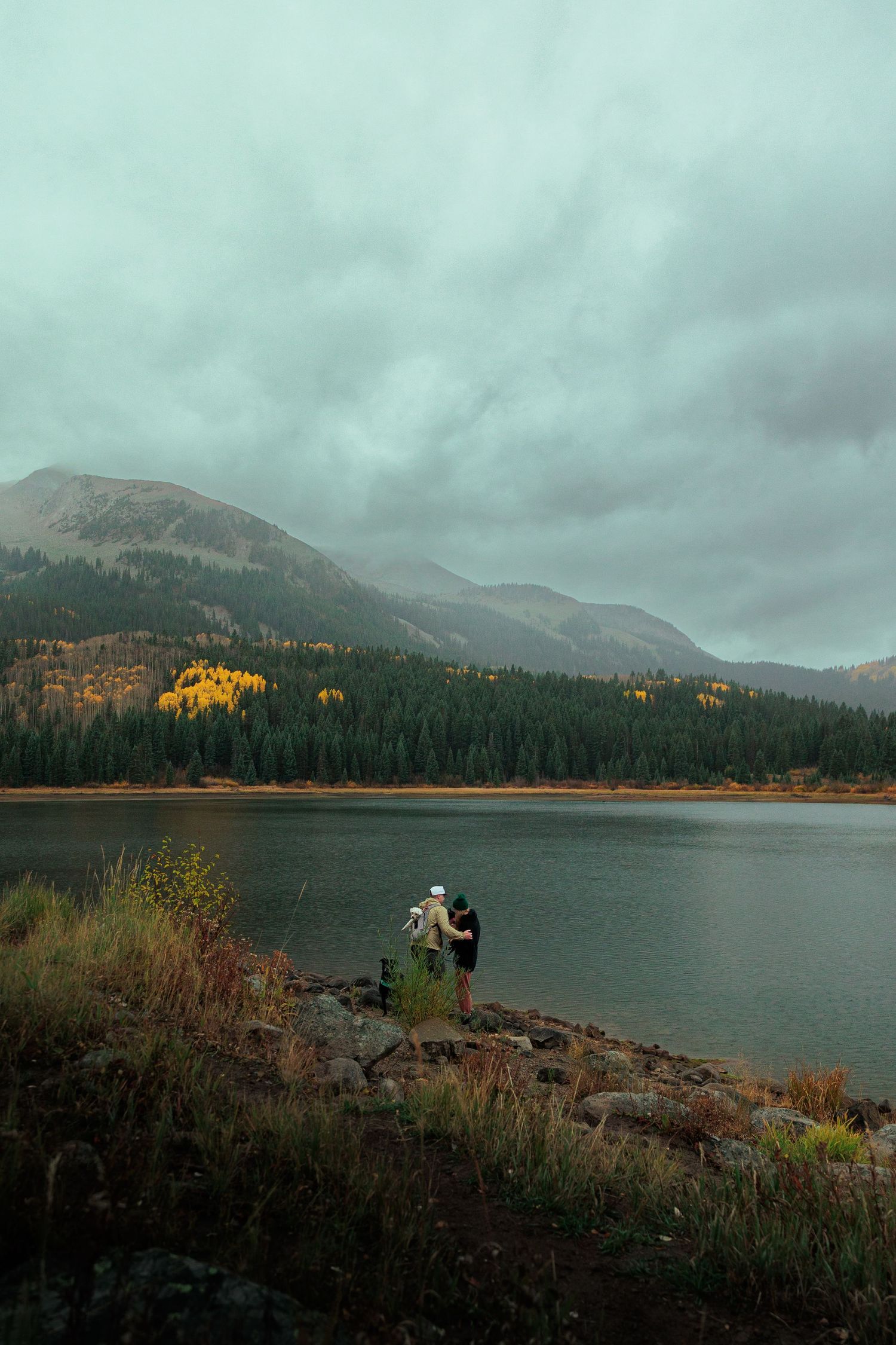Scenic mountain lake surrounded by evergreen forest and autumn colors under cloudy skies.