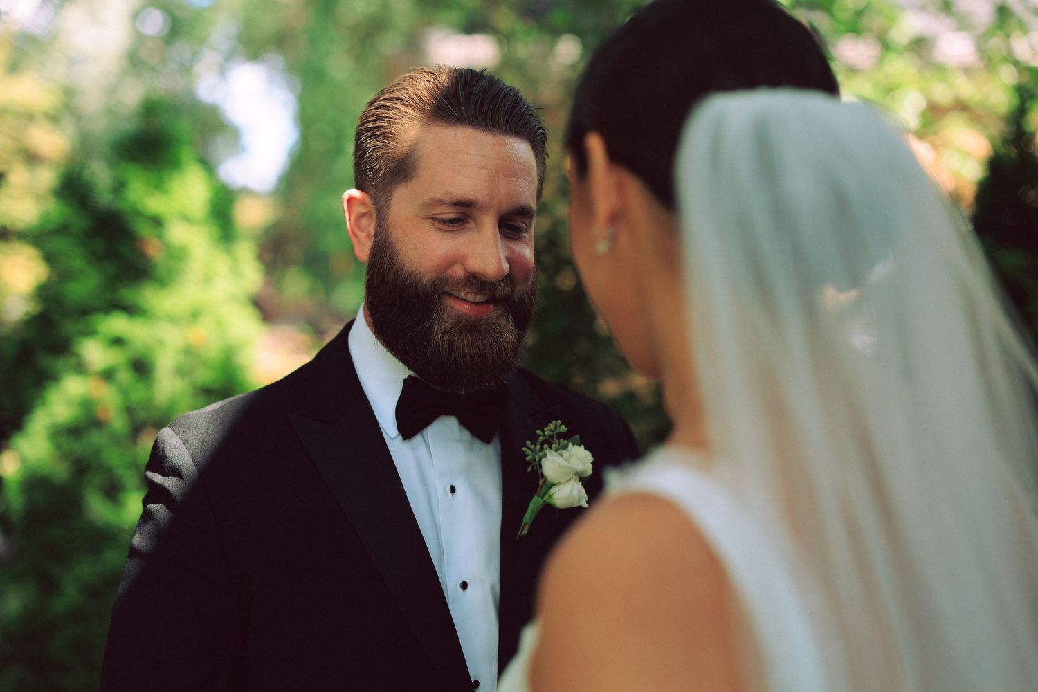 Couple shares tender moment during outdoor wedding photoshoot among trees.