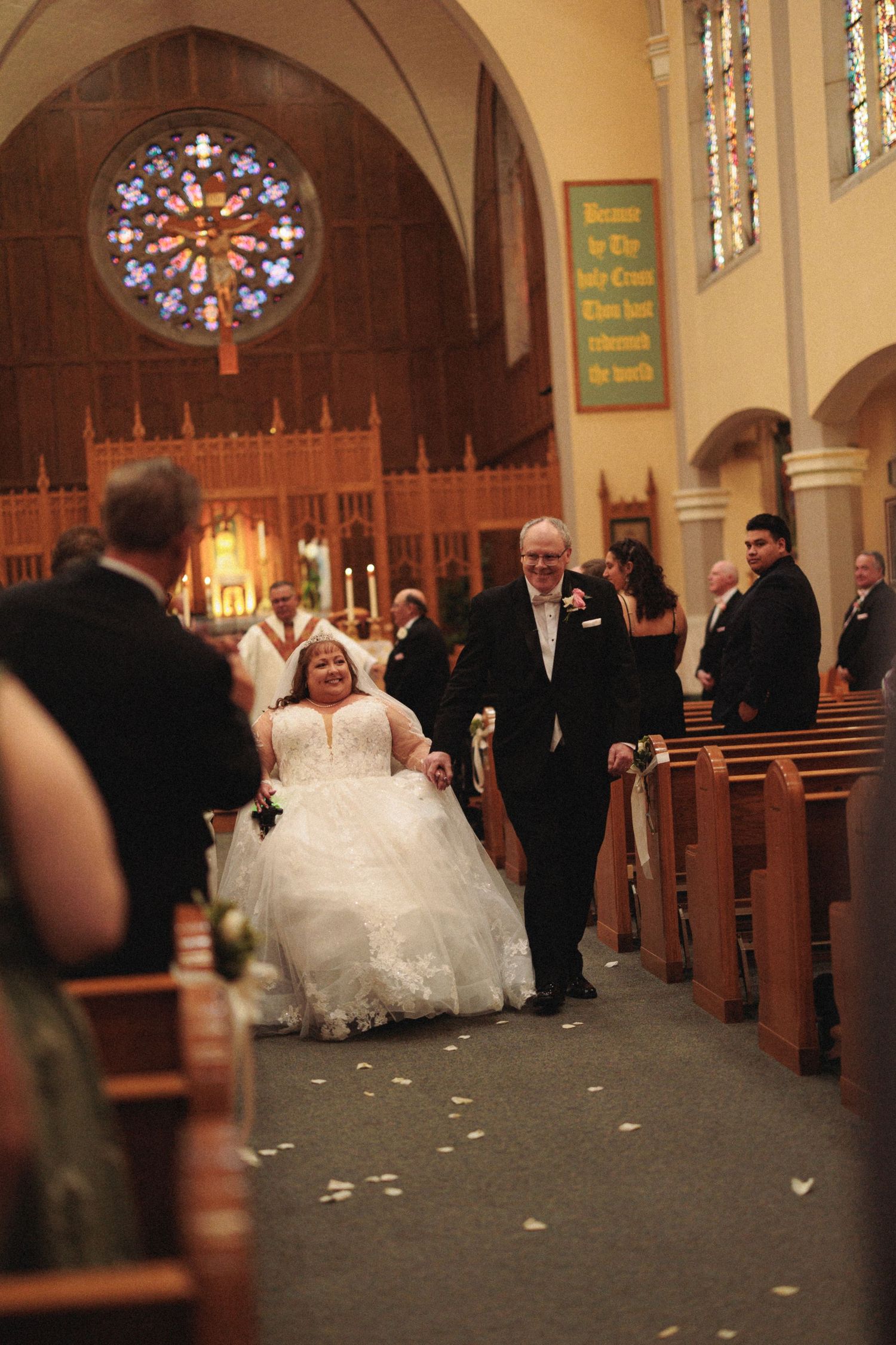 A wedding ceremony procession walking down the aisle of a church with stained glass windows.