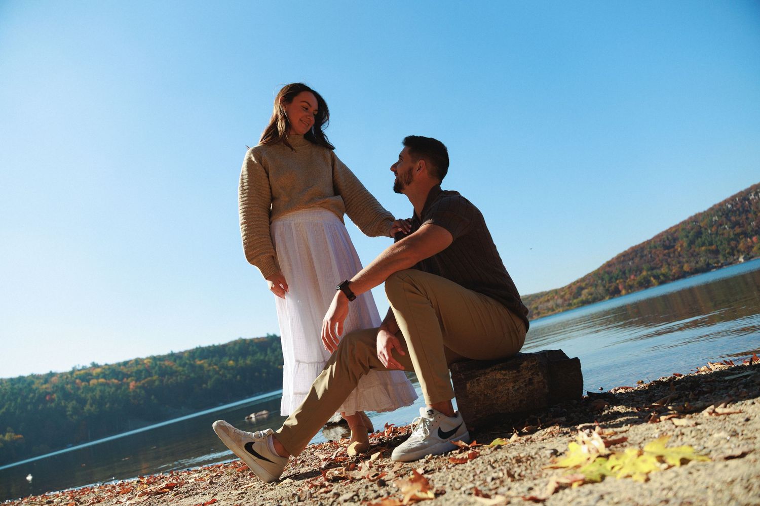 Couple sitting together on a sunny beach shoreline with clear blue skies.