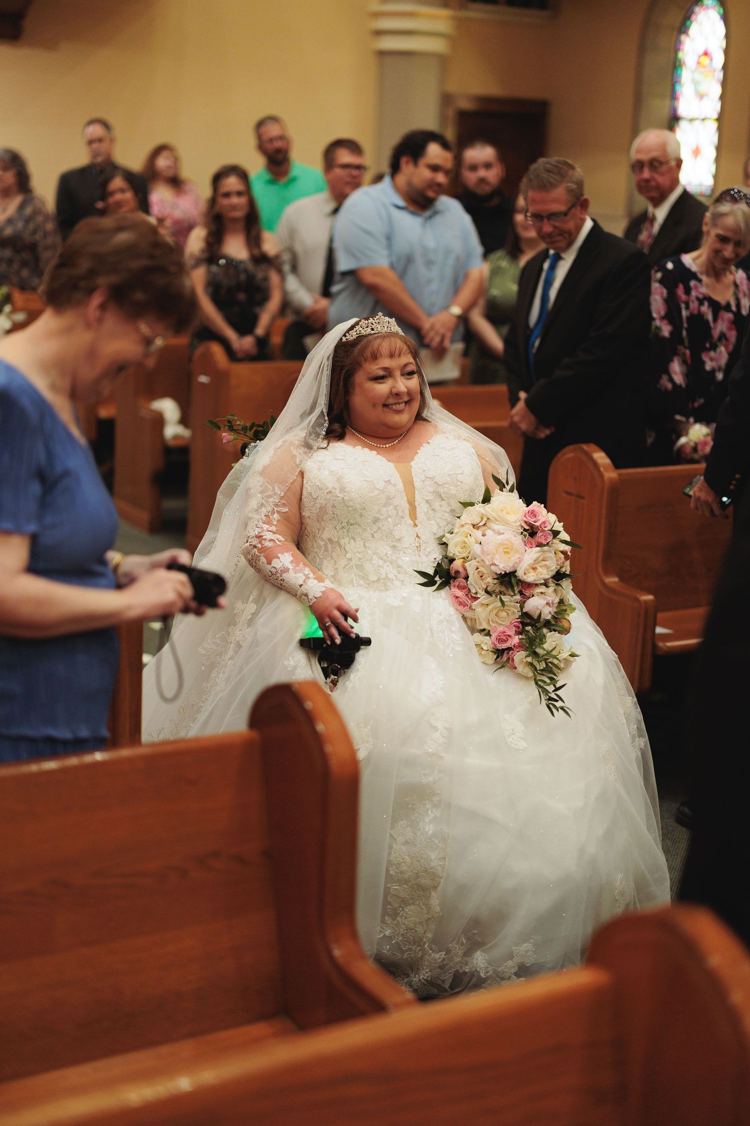 Bride in white lace gown celebrates joyfully in church pews during ceremony.
