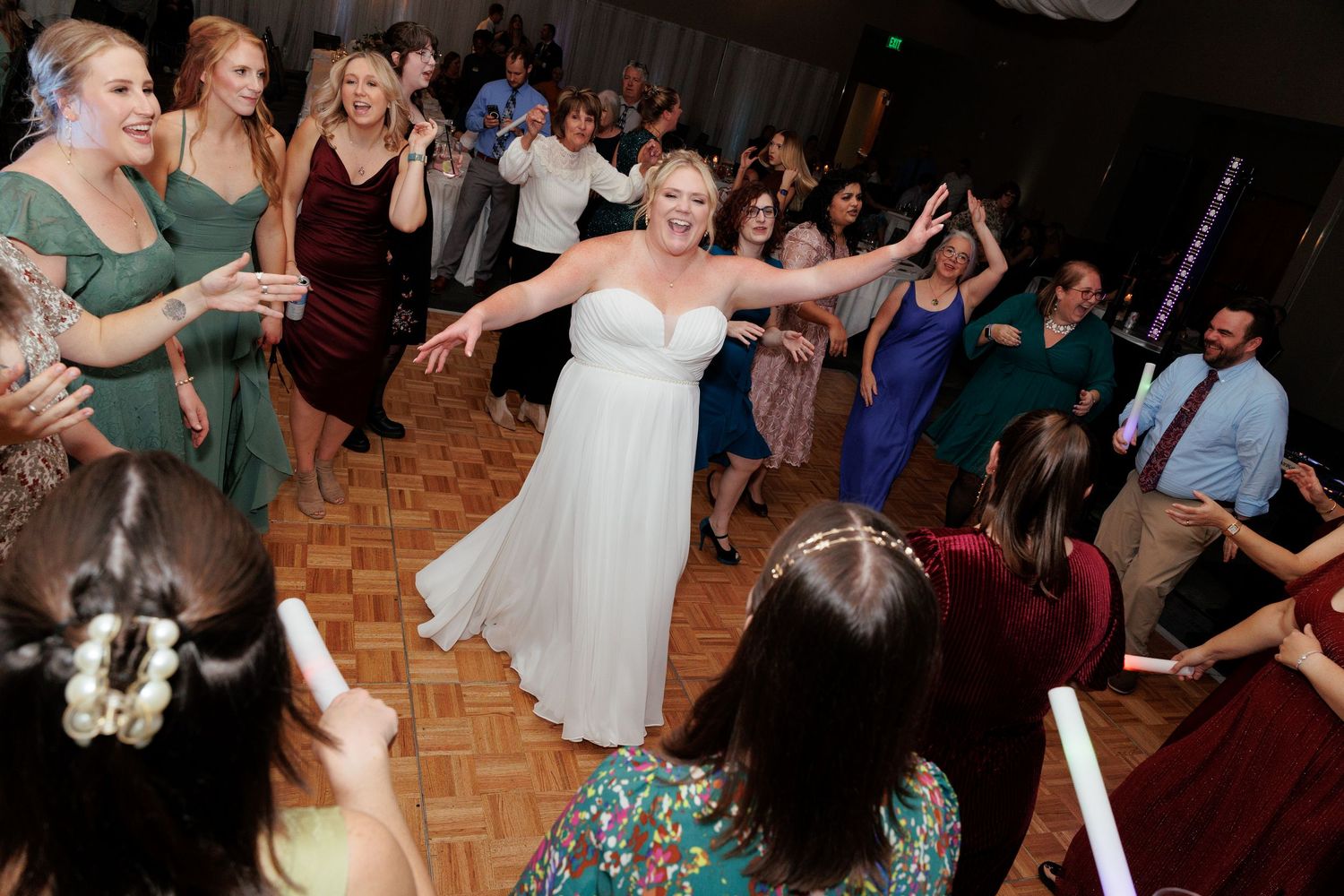 Wedding guests dancing and celebrating on a wooden dance floor during reception.
