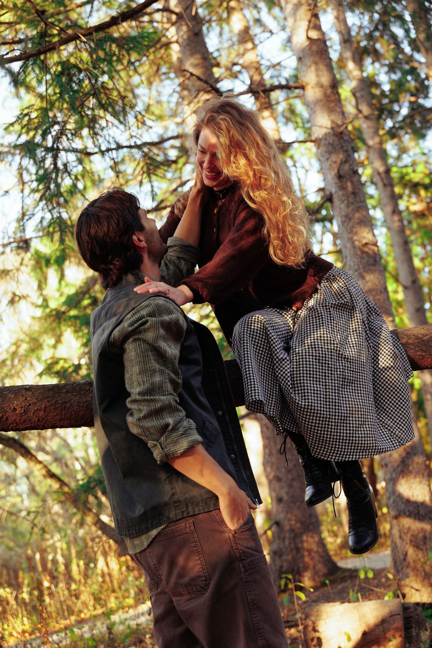 Couple sharing a playful moment on a wooden bench surrounded by sunlit trees.