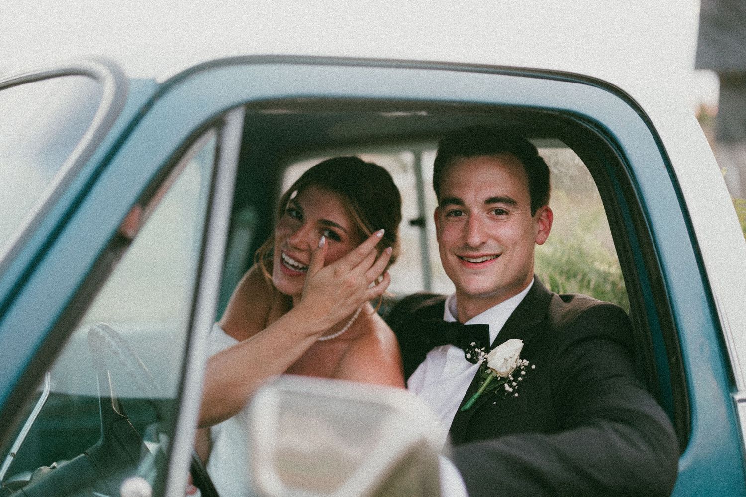 Wedding couple in vintage car sharing joyful moment after ceremony.