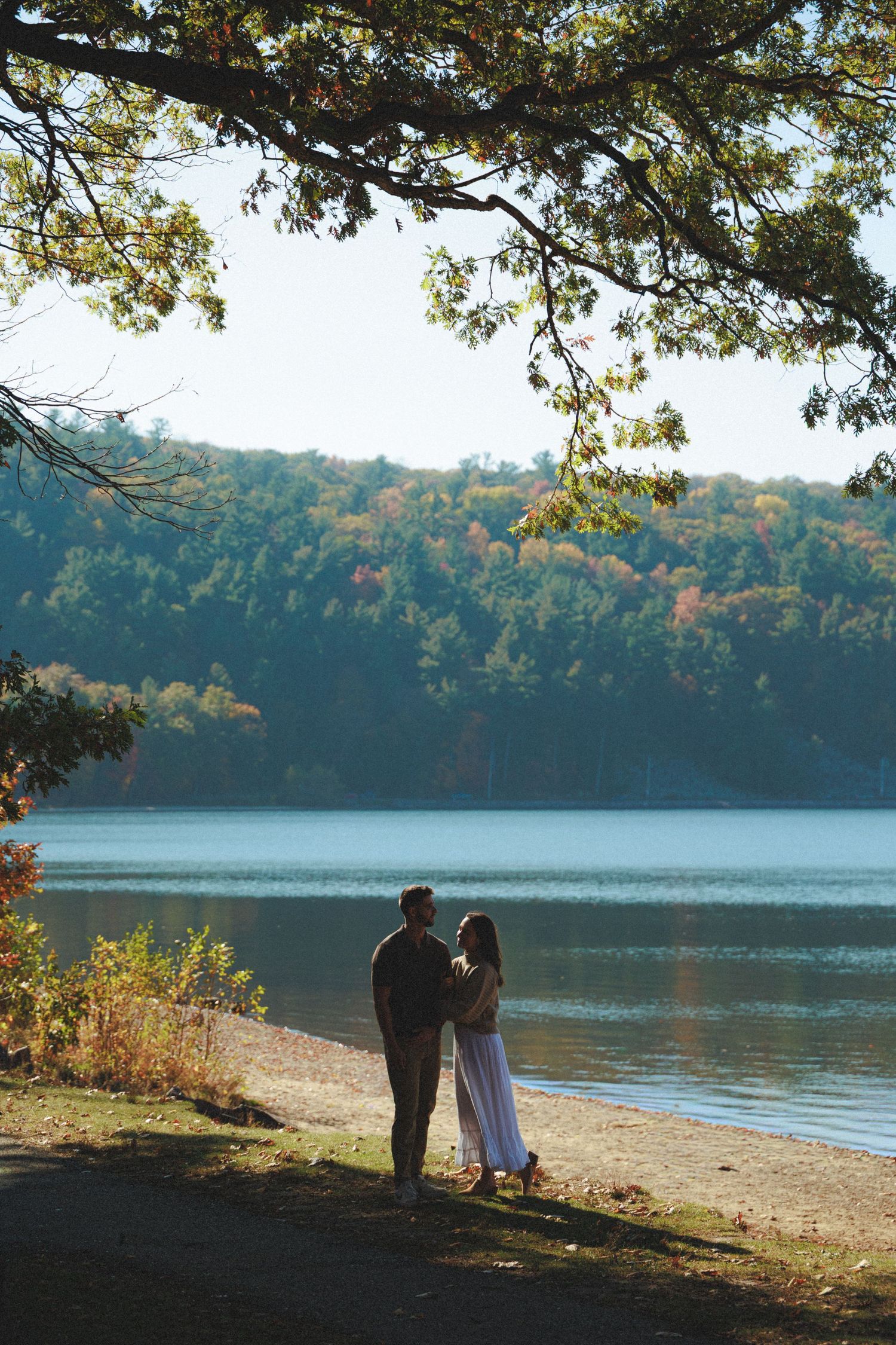 Silhouetted couple standing by lake shore during autumn sunset.