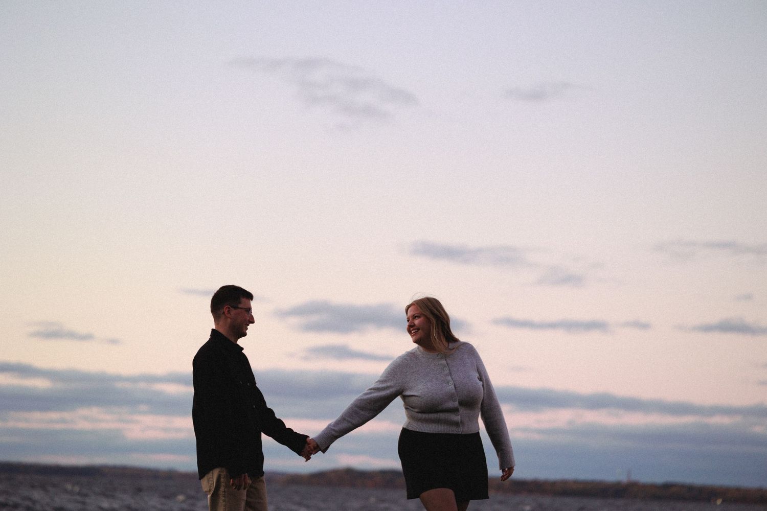 Couple walking together on a dock at dusk with cloudy skies.