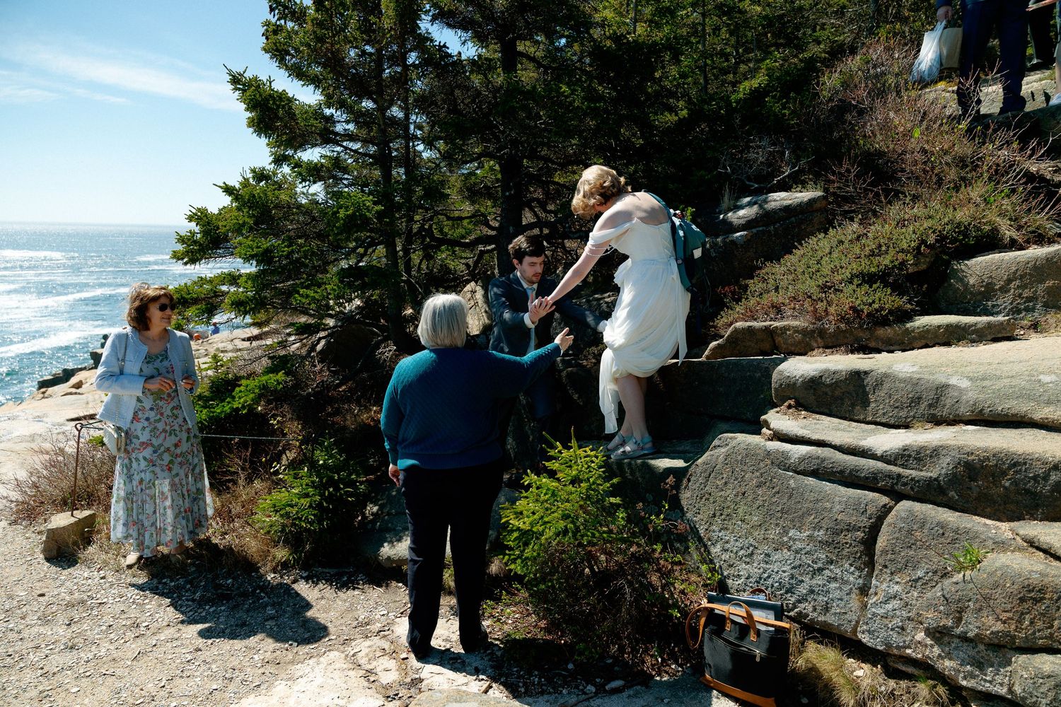 Wedding party gathering on rocky coastal cliff overlooking ocean during outdoor ceremony.