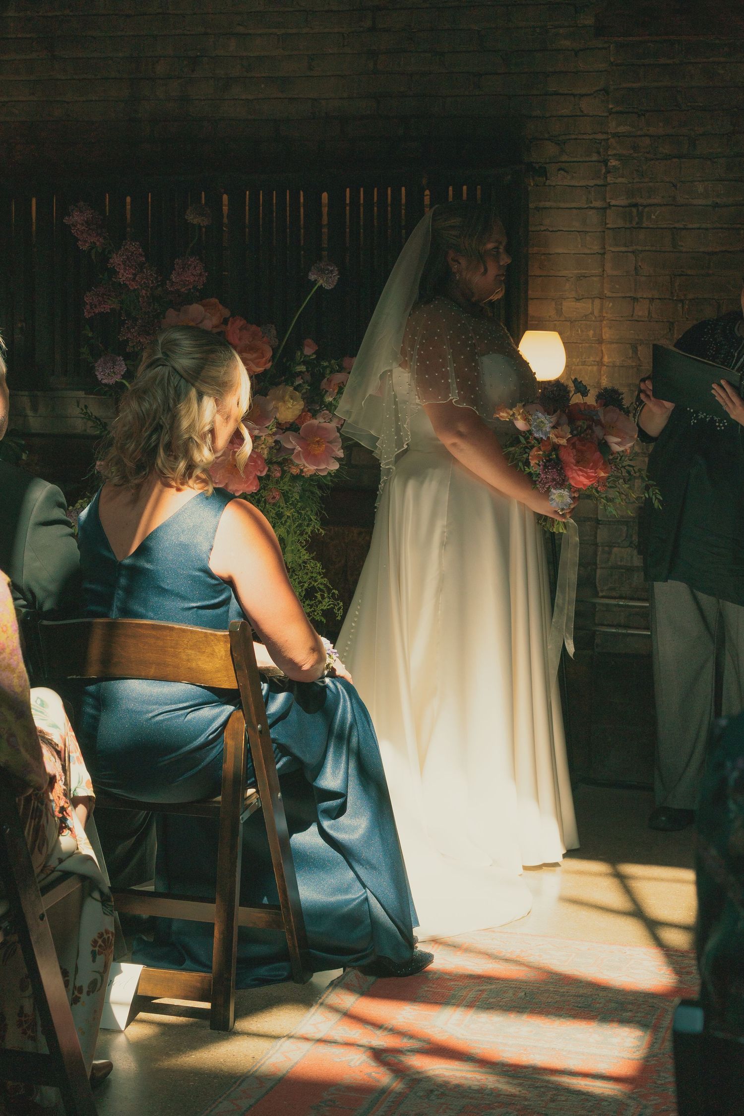 Wedding photographer capturing moments in dramatic lighting against brick wall.
