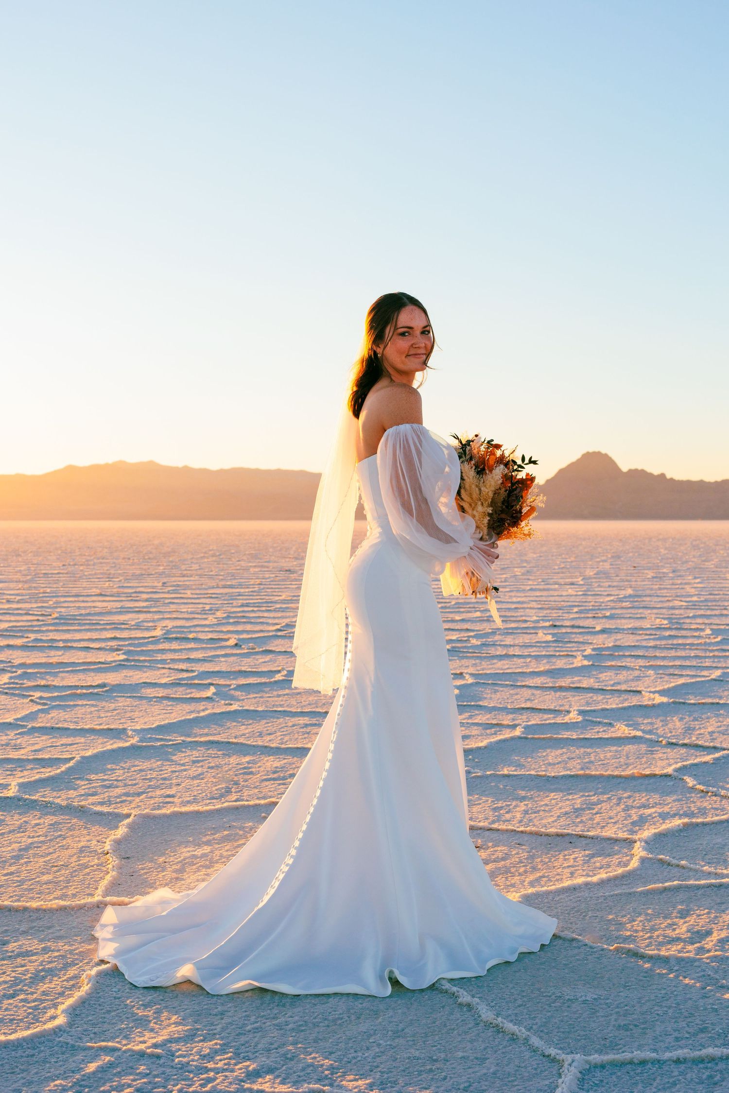 Bride in flowing white dress poses on crystalline utah salt flats at golden hour.