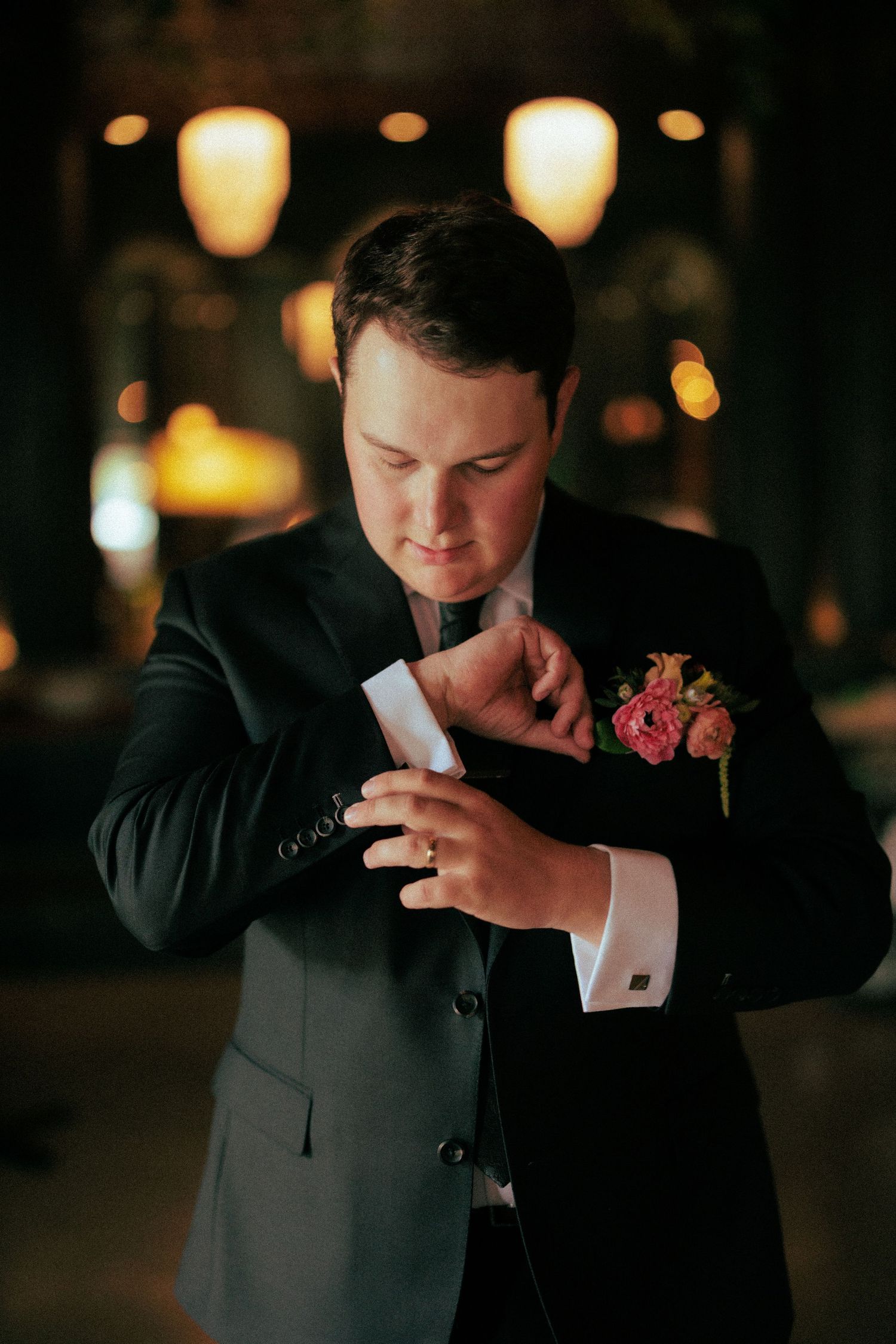 Emotional groom in a dark suit wipes tears during wedding ceremony in dimly lit venue.