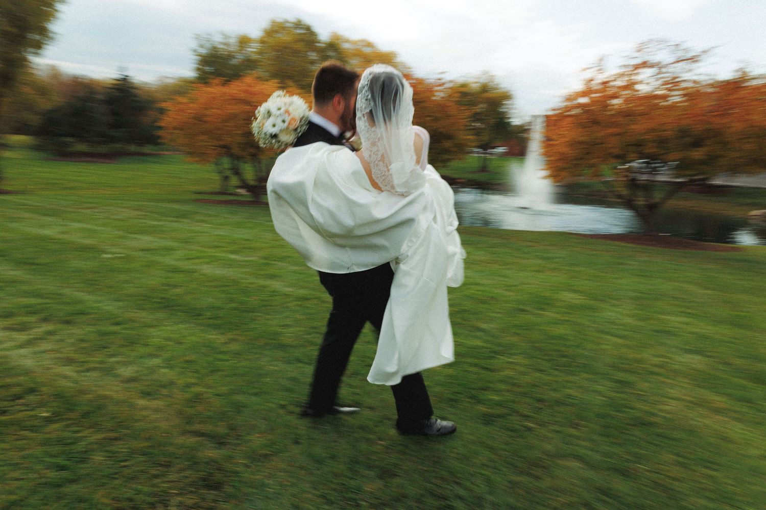 Playful wedding couple spinning and dancing on grass during outdoor photo session.