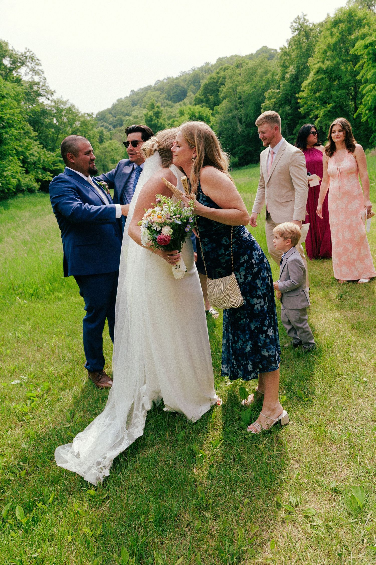 Wedding guests gather in a sunny meadow to celebrate with the newlyweds.