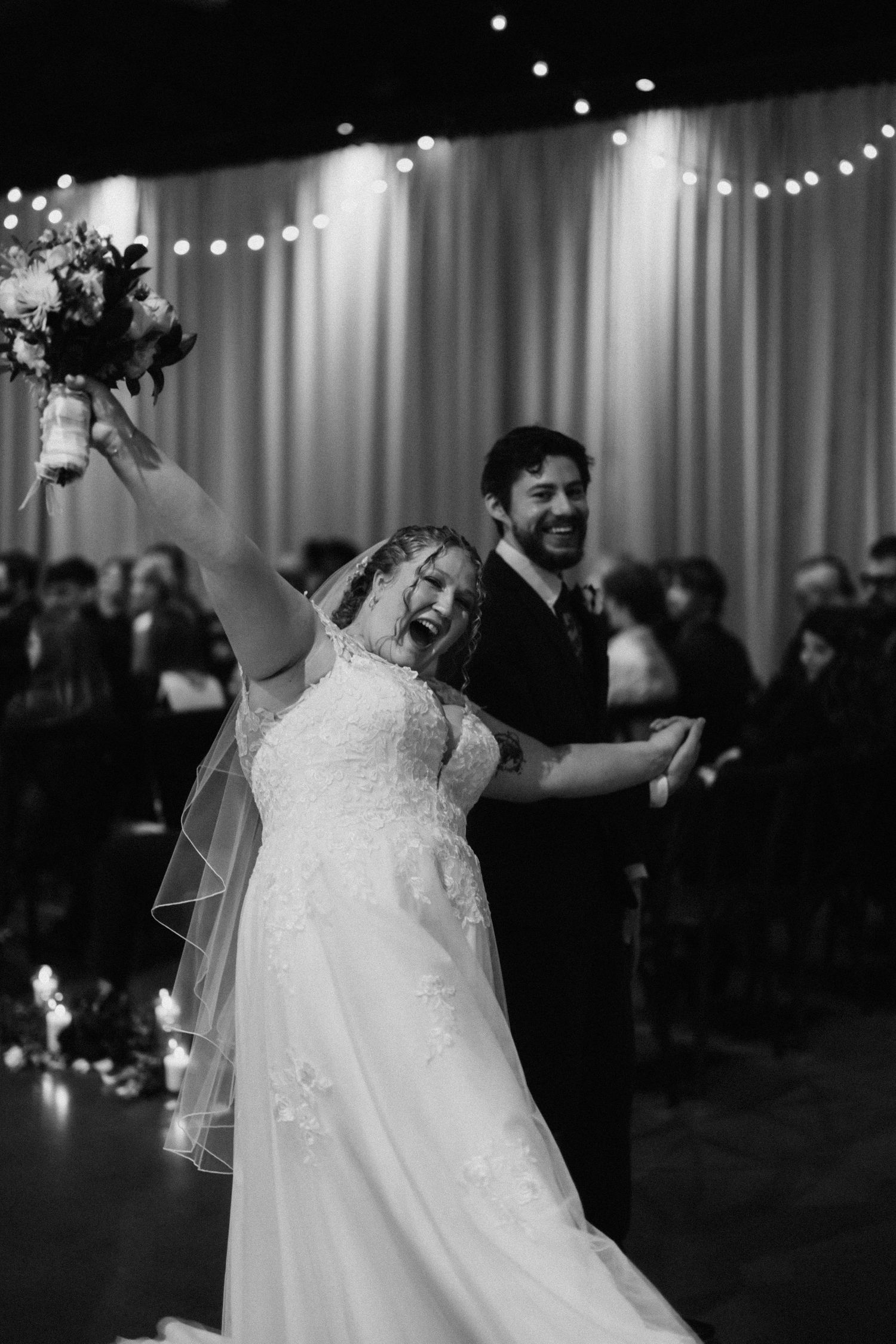 Bride celebrates joyfully on the dance floor under twinkling reception lights.