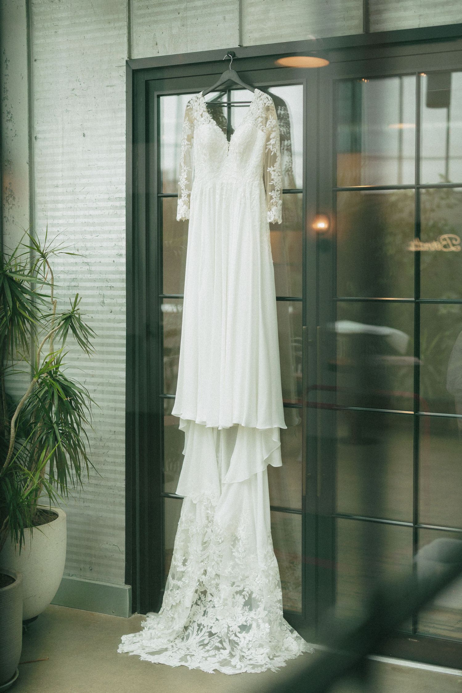 Elegant white lace wedding dress hanging on display in modern interior with brick walls.