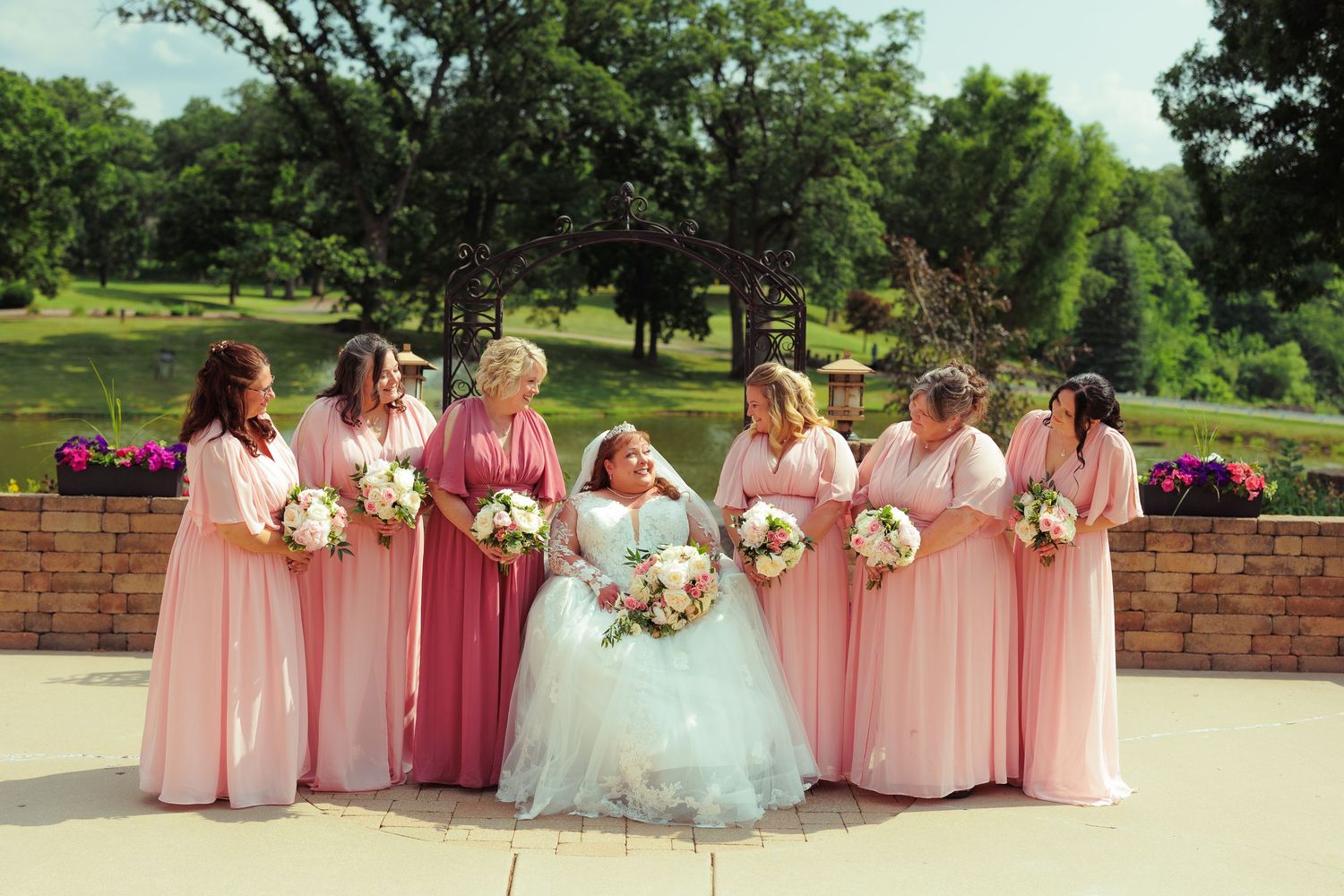 Bridesmaids in pink dresses pose with bouquets in an outdoor garden setting.